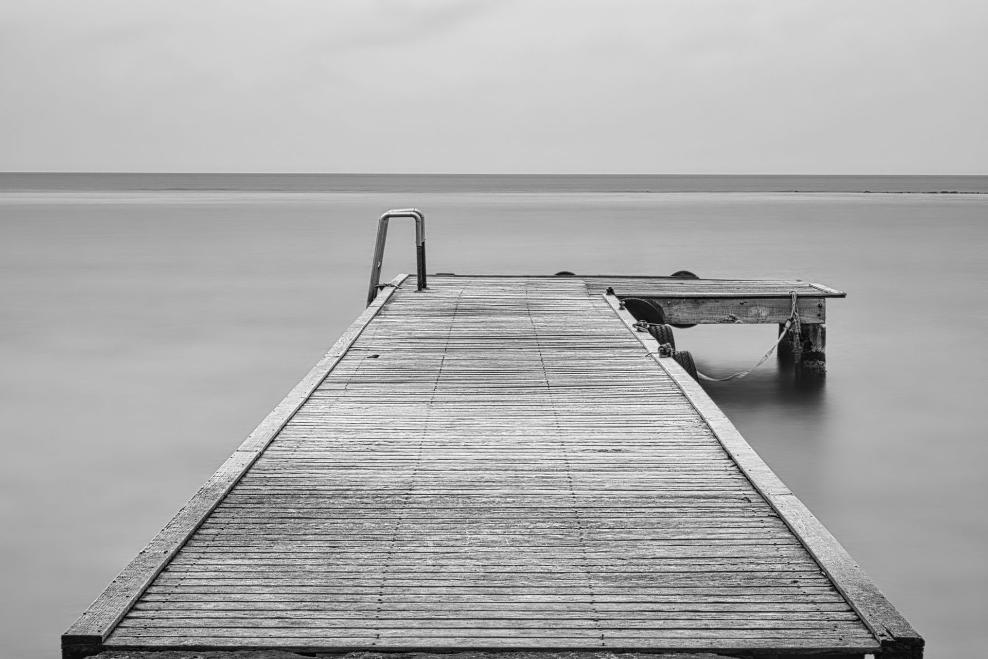 Wooden pier extending into calm water, with a small ladder and side platform under a gray sky