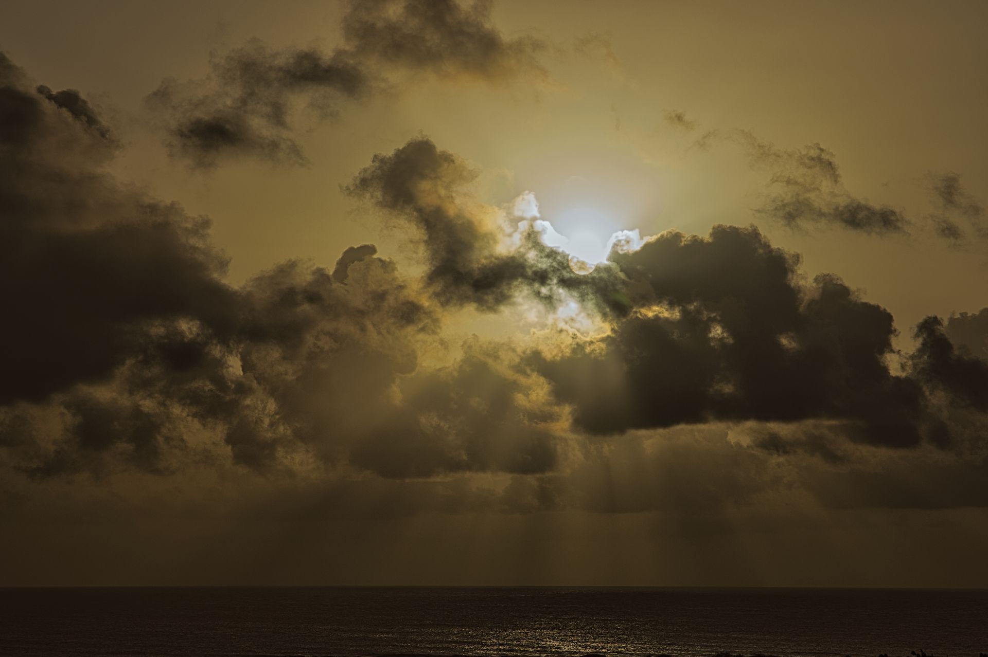 Sun breaking through dark clouds over a calm sea at sunset