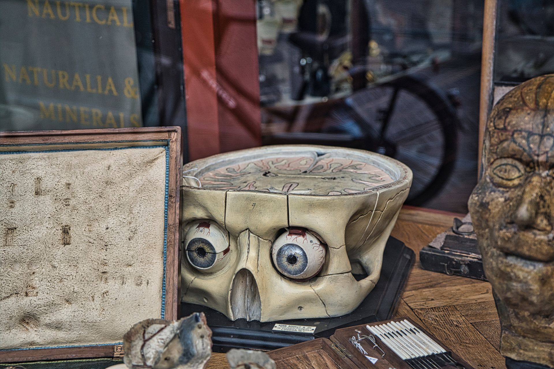 Vintage shop display with a ceramic face planter, framed board, and carved stone head on a wooden table