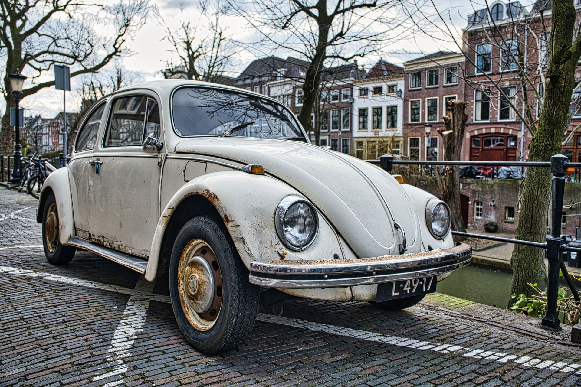 Classic white Volkswagen Beetle parked on a cobblestone street beside a canal and historic buildings