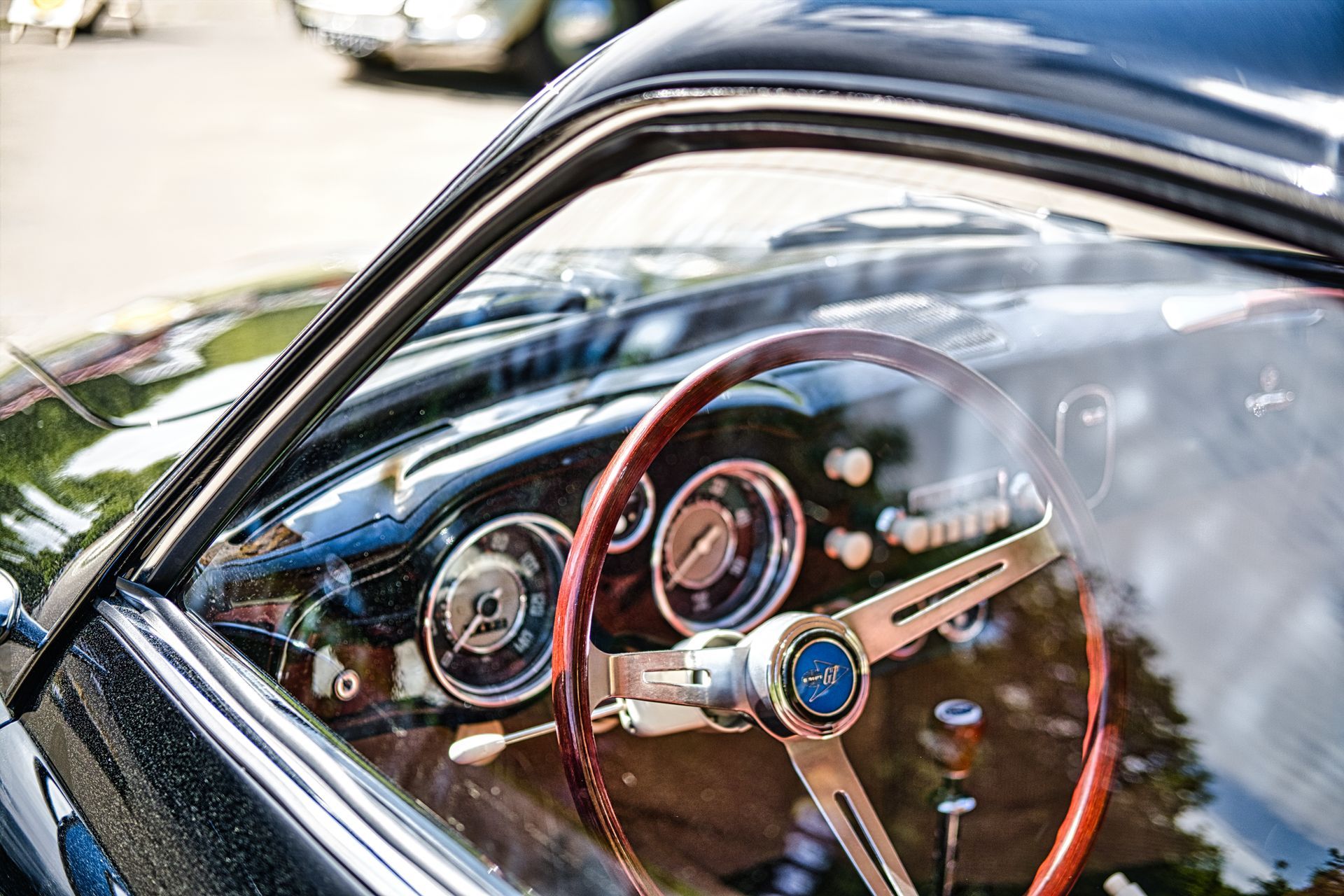 Classic car interior with wooden steering wheel and chrome dashboard reflected in the windshield
