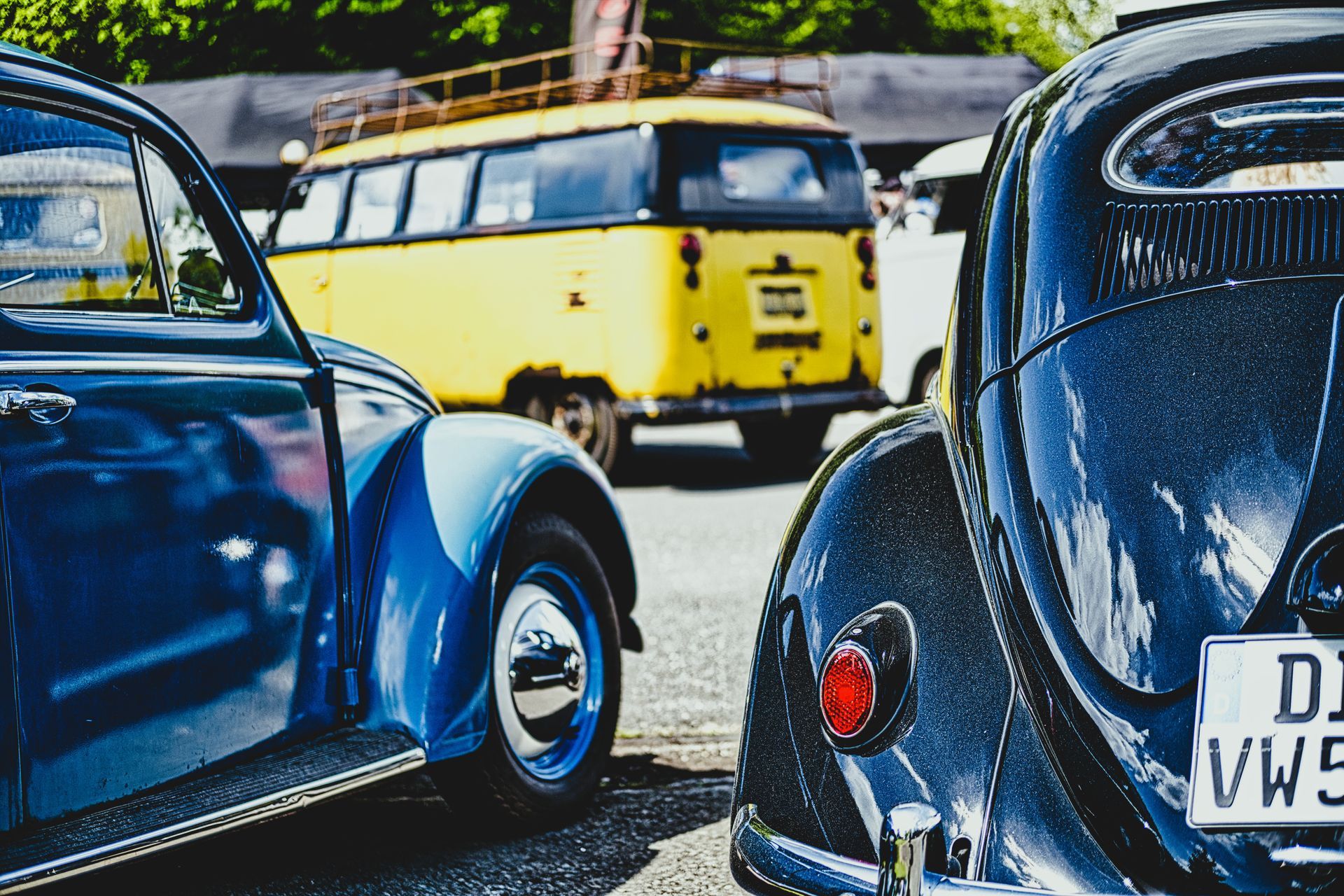 Three vintage cars parked close together, including a yellow van and blue and black Beetles.