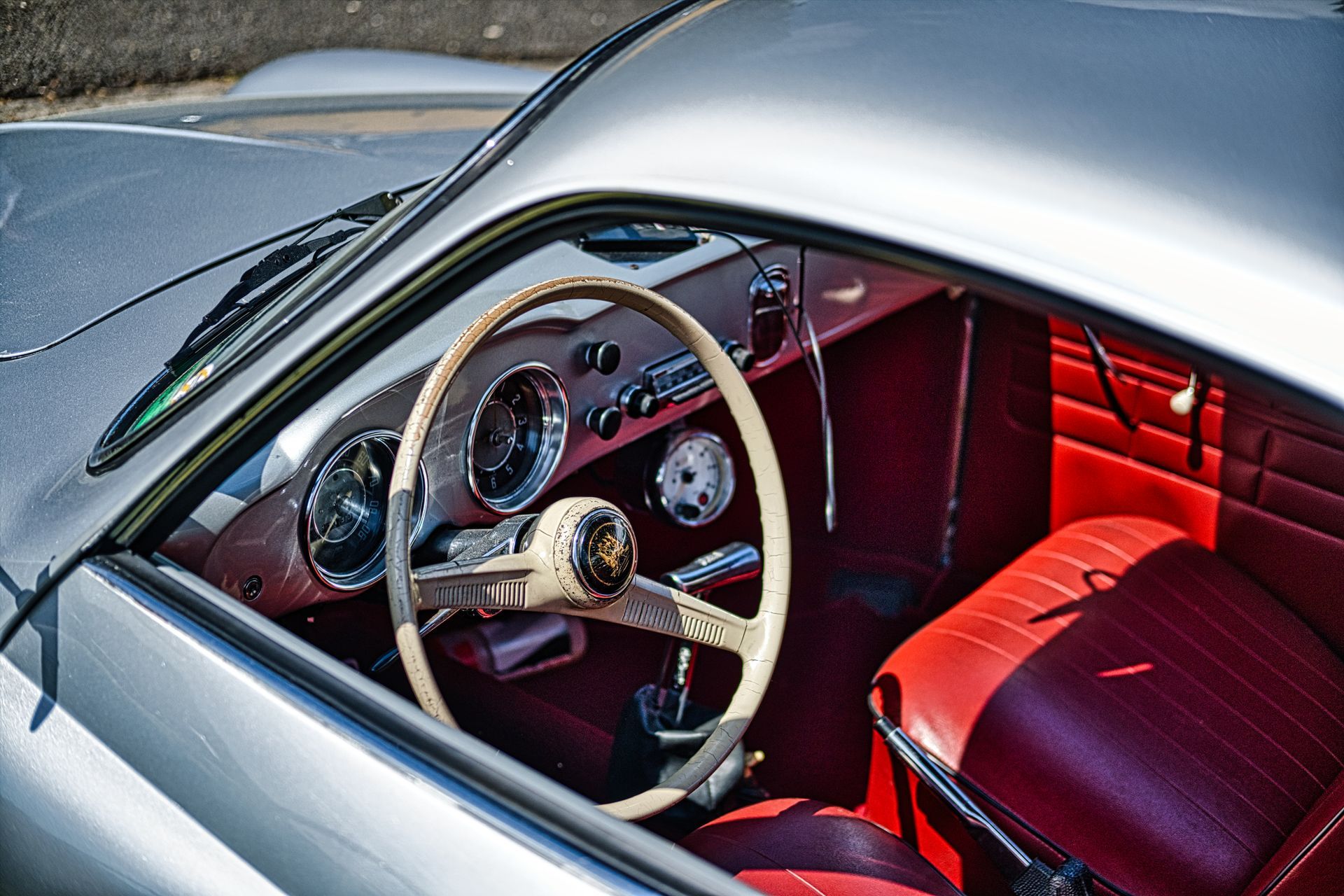 Vintage car interior with red seats, wood steering wheel, and dashboard gauges viewed through the open window