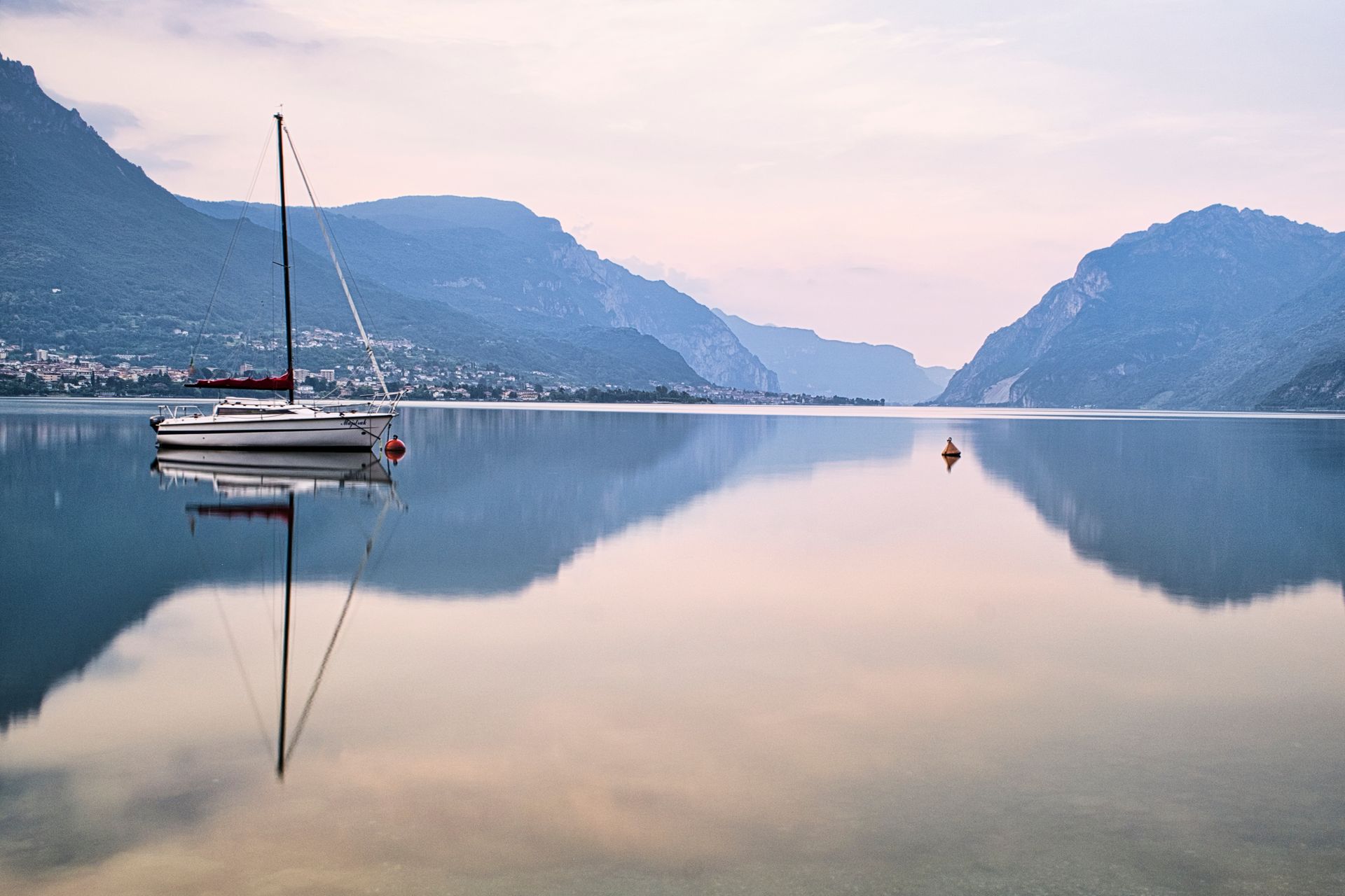 Sailboat on calm lake at sunrise, with mountain reflections in the water