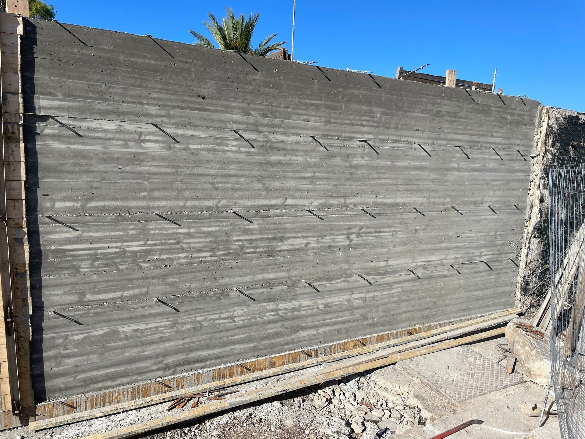 Muro di stucco grigio in un cantiere edile con cielo azzurro sopra e macerie alla base.