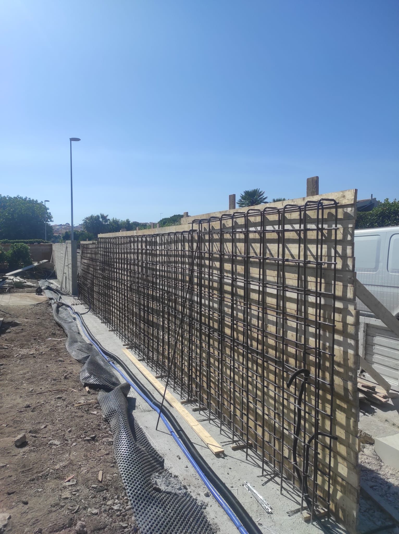 Cantiere edile con una lunga fila di gabbie di armatura lungo una fondazione in cemento sotto un cielo azzurro