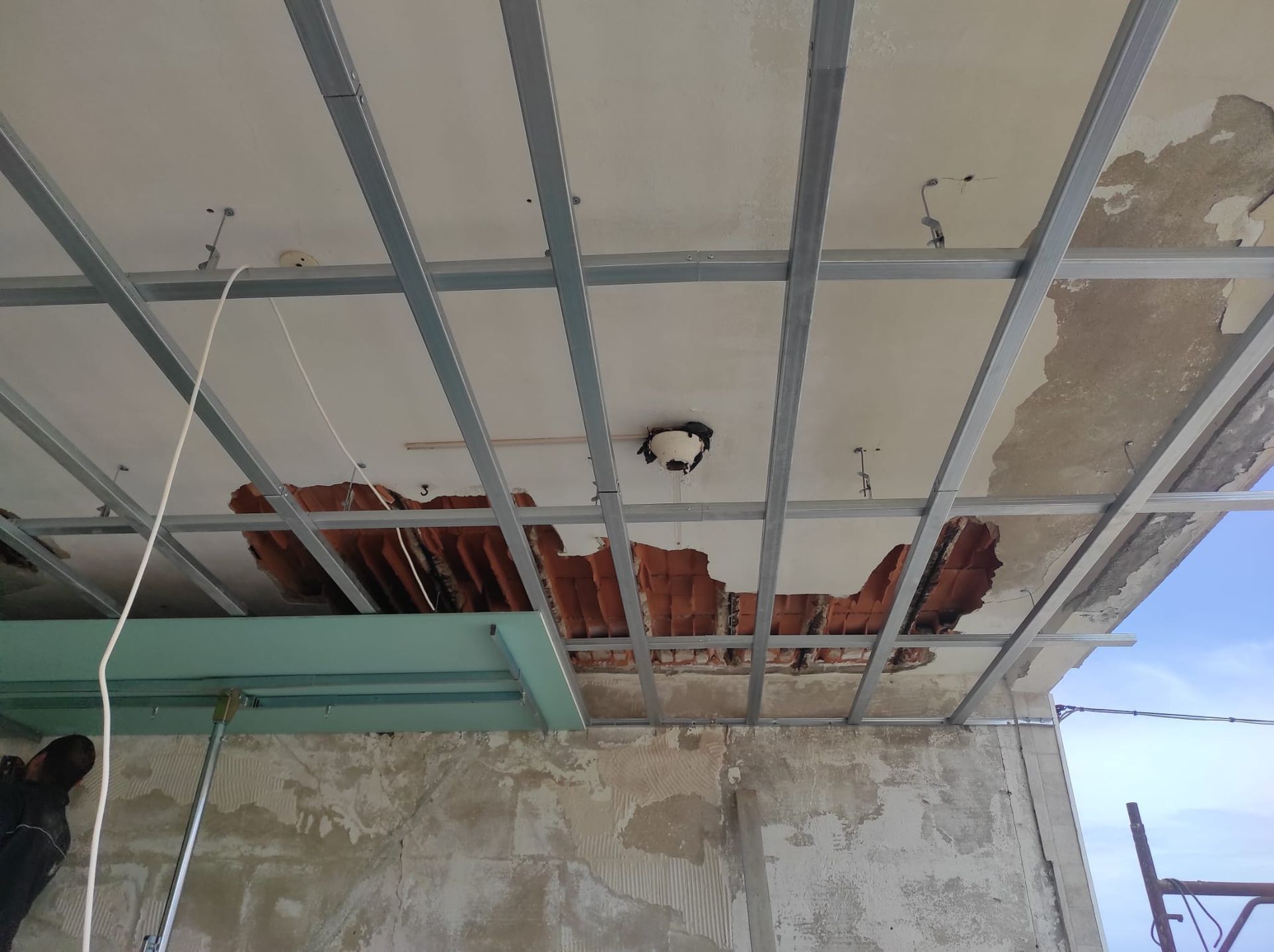Soffitto danneggiato con isolamento rosso a vista e struttura metallica in una stanza in fase di ristrutturazione.