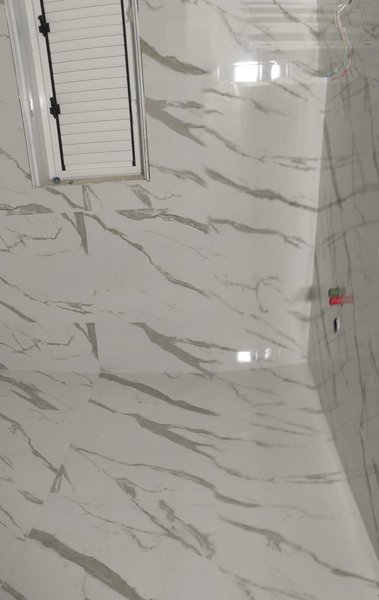 Bagno con pareti e pavimento rivestiti in marmo, zona doccia e piccolo lampadario a parete.