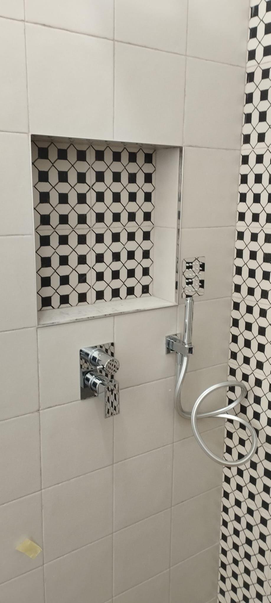 Parete della doccia del bagno con nicchia piastrellata, comandi cromati e doccetta a mano.