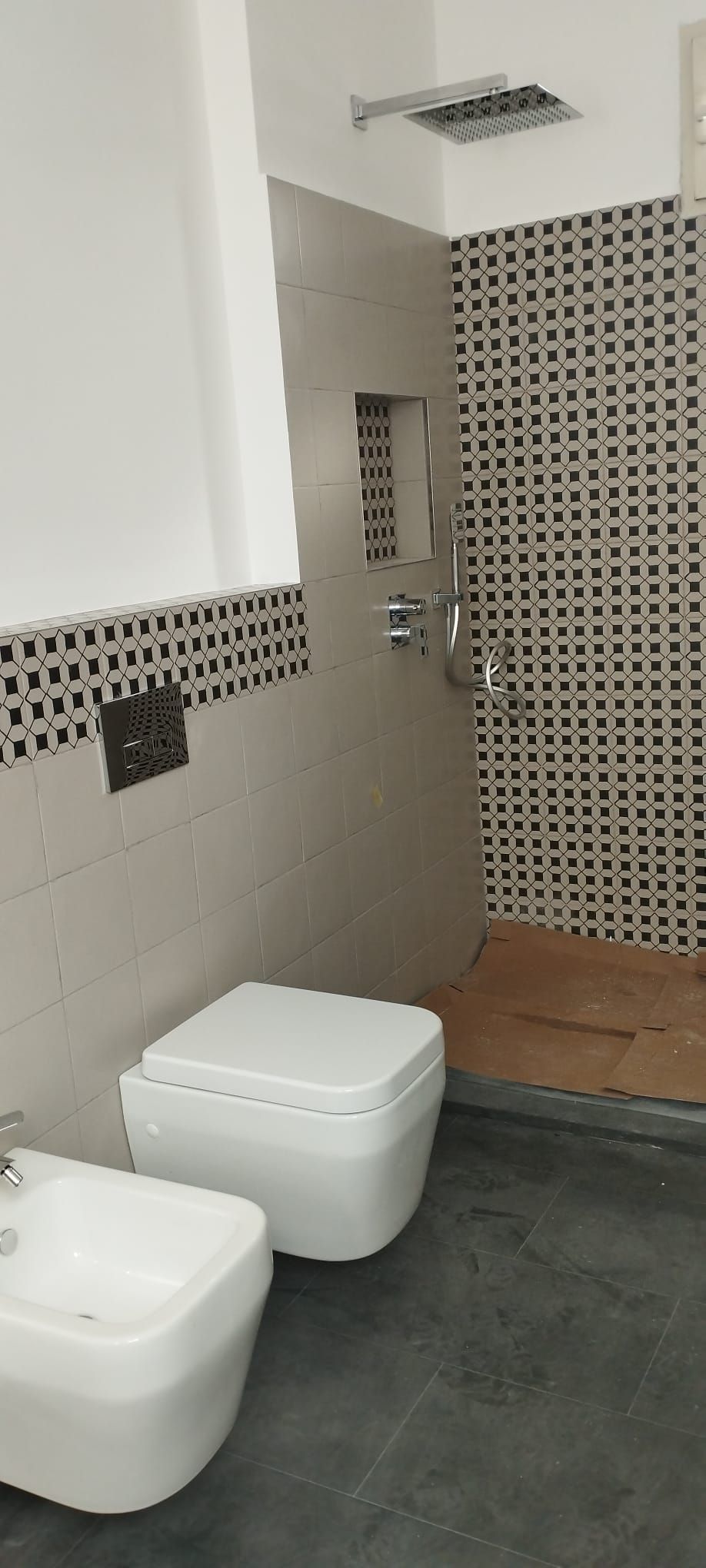 Bagno moderno con sanitari bianchi, pavimento in piastrelle grigie e parete decorativa con motivo decorativo.