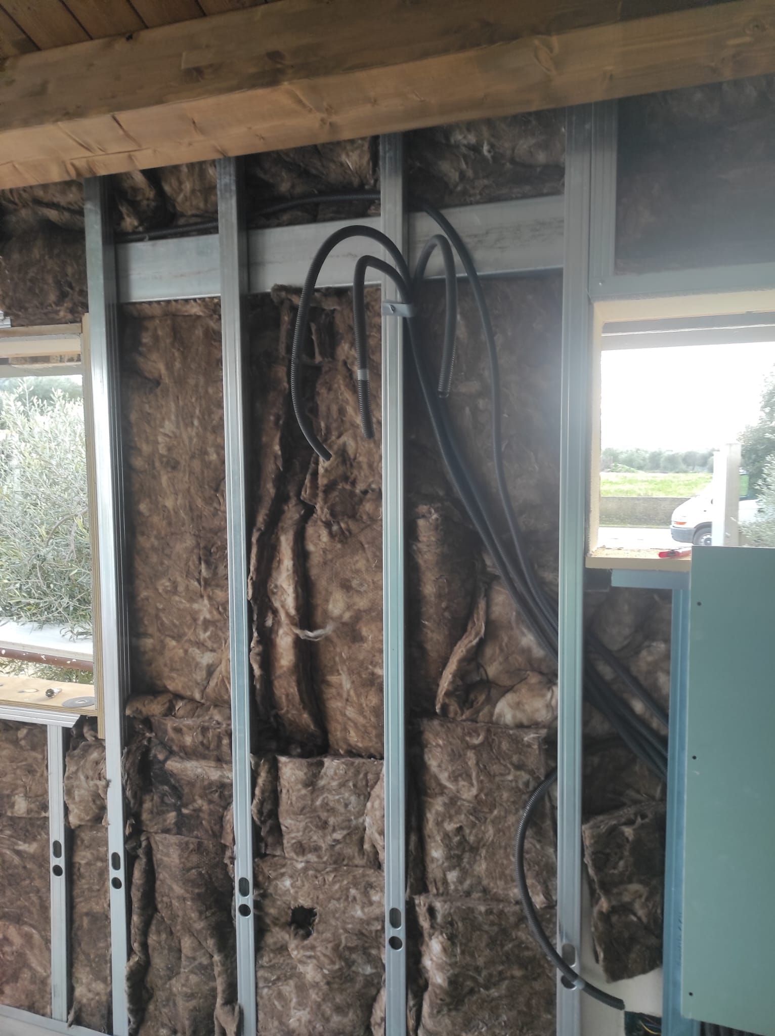 Struttura di parete parzialmente isolata con montanti a vista, cavi elettrici e apertura per una finestra in una stanza in costruzione.
