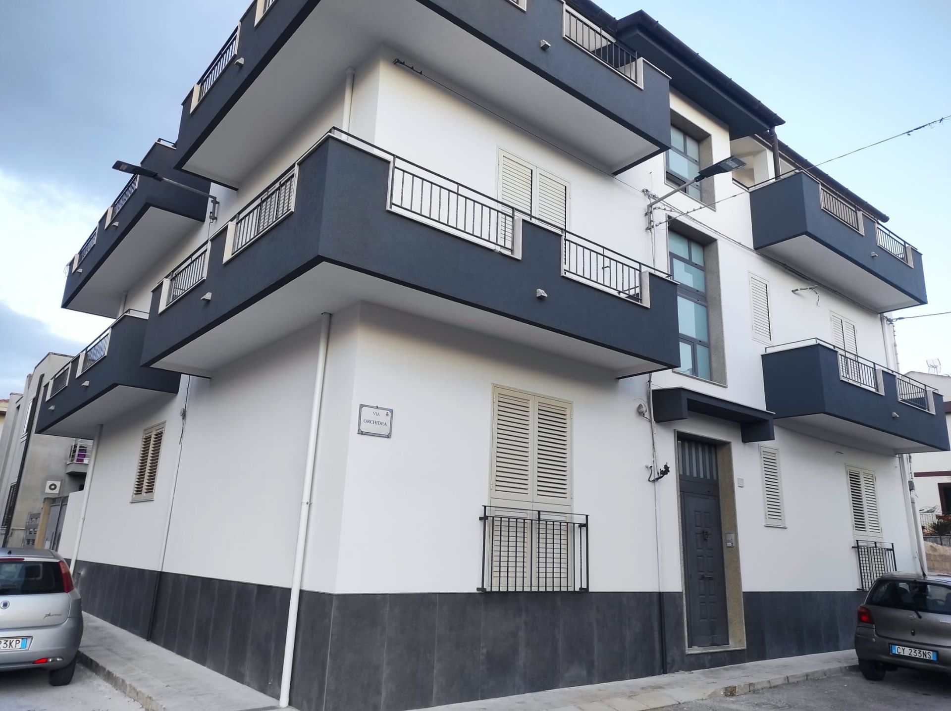 Moderno condominio grigio e bianco all'angolo di una strada con auto parcheggiate nelle vicinanze.