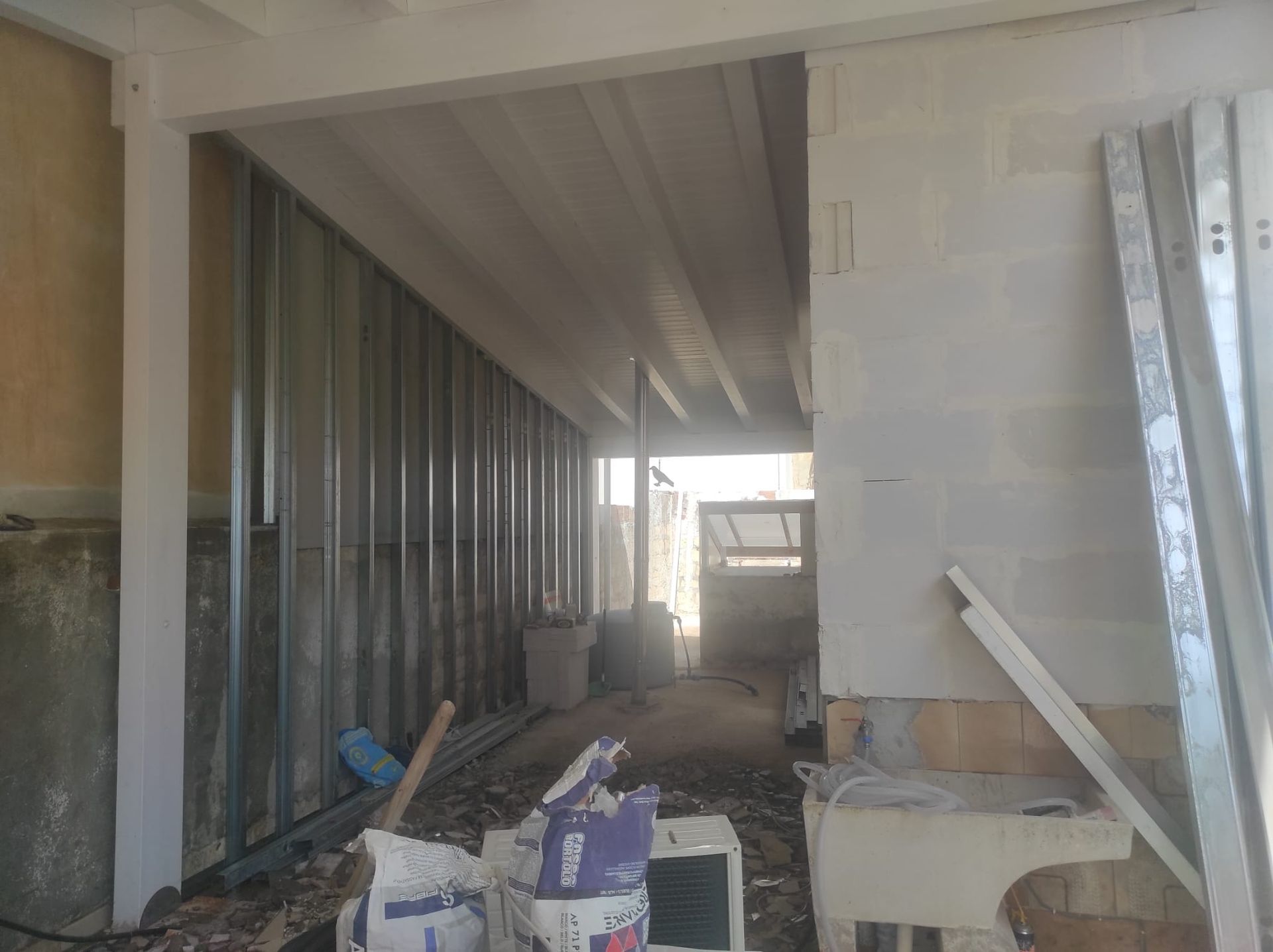 Interno parzialmente allestito con struttura metallica delle pareti, soffitto a vista e materiali da costruzione sul pavimento.