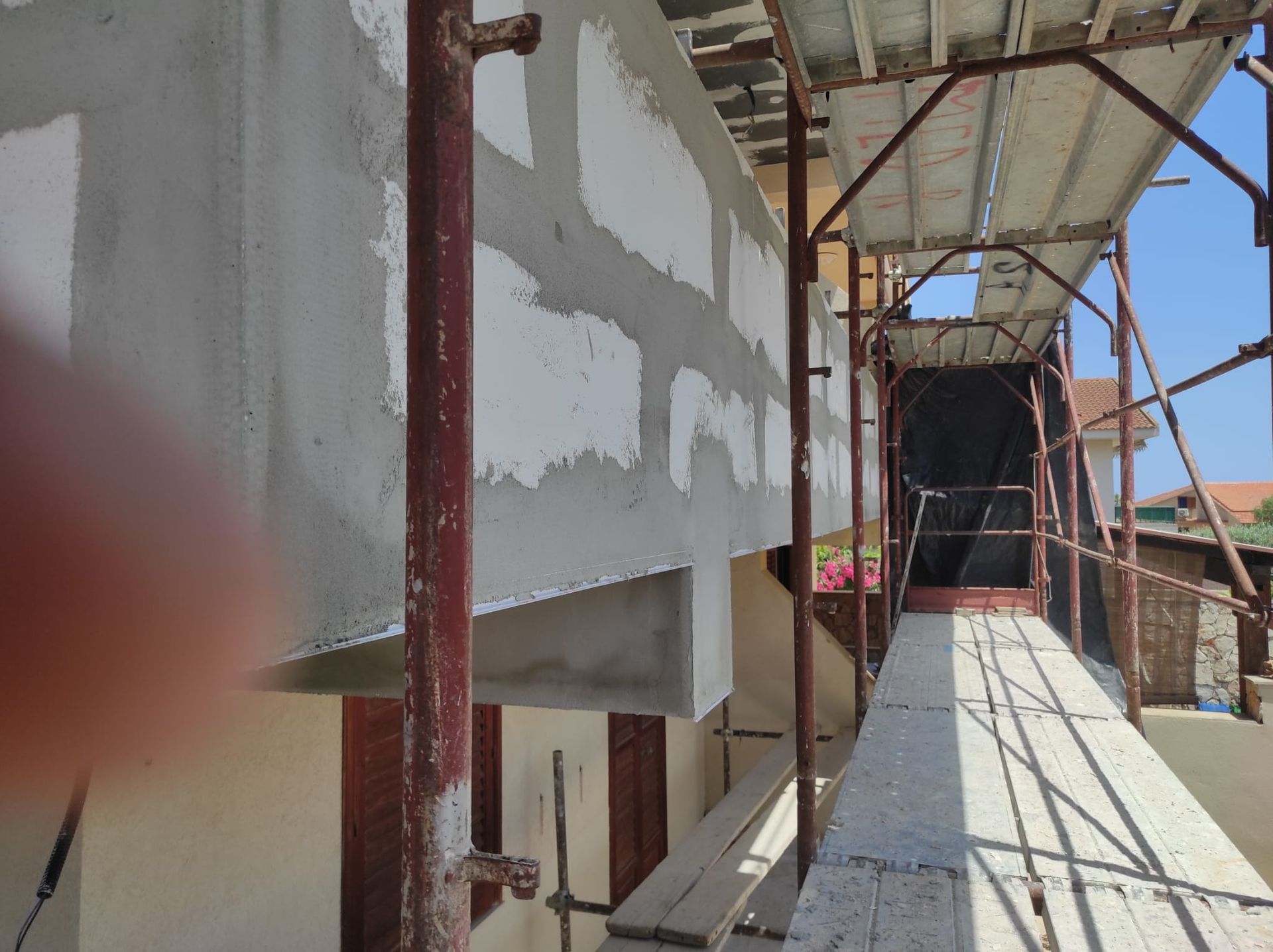 Impalcature a fianco di un edificio in costruzione, con pareti intonacate e una passerella di legno.