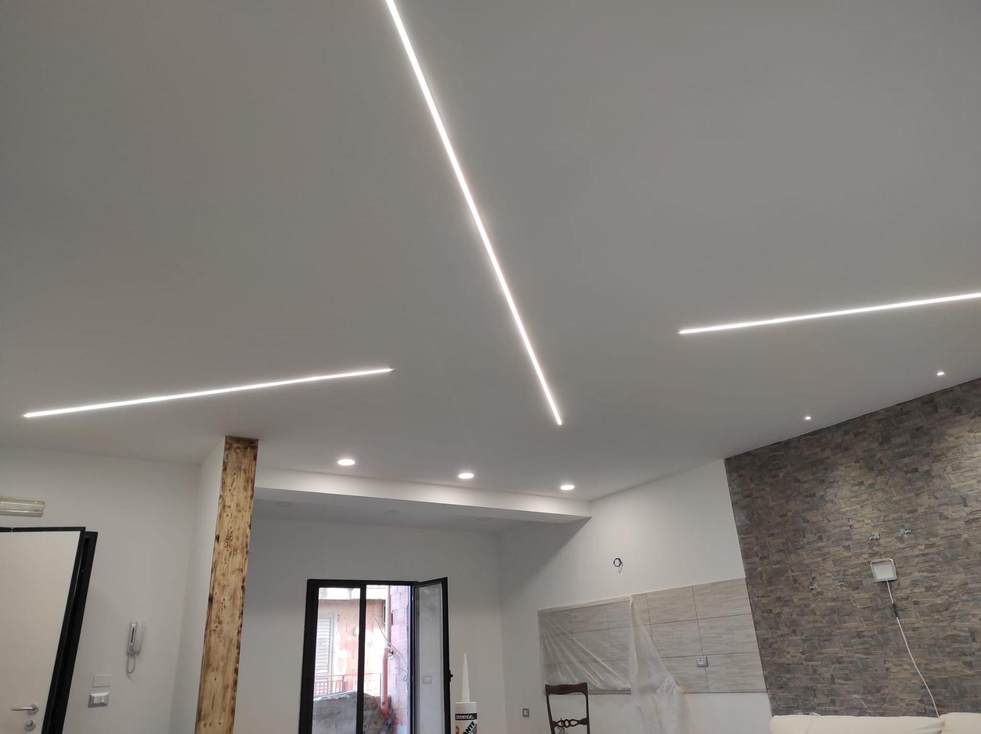 Stanza moderna in fase di ristrutturazione con faretti a LED a incasso, soffitto bianco, pareti grigie e parete decorativa in pietra.