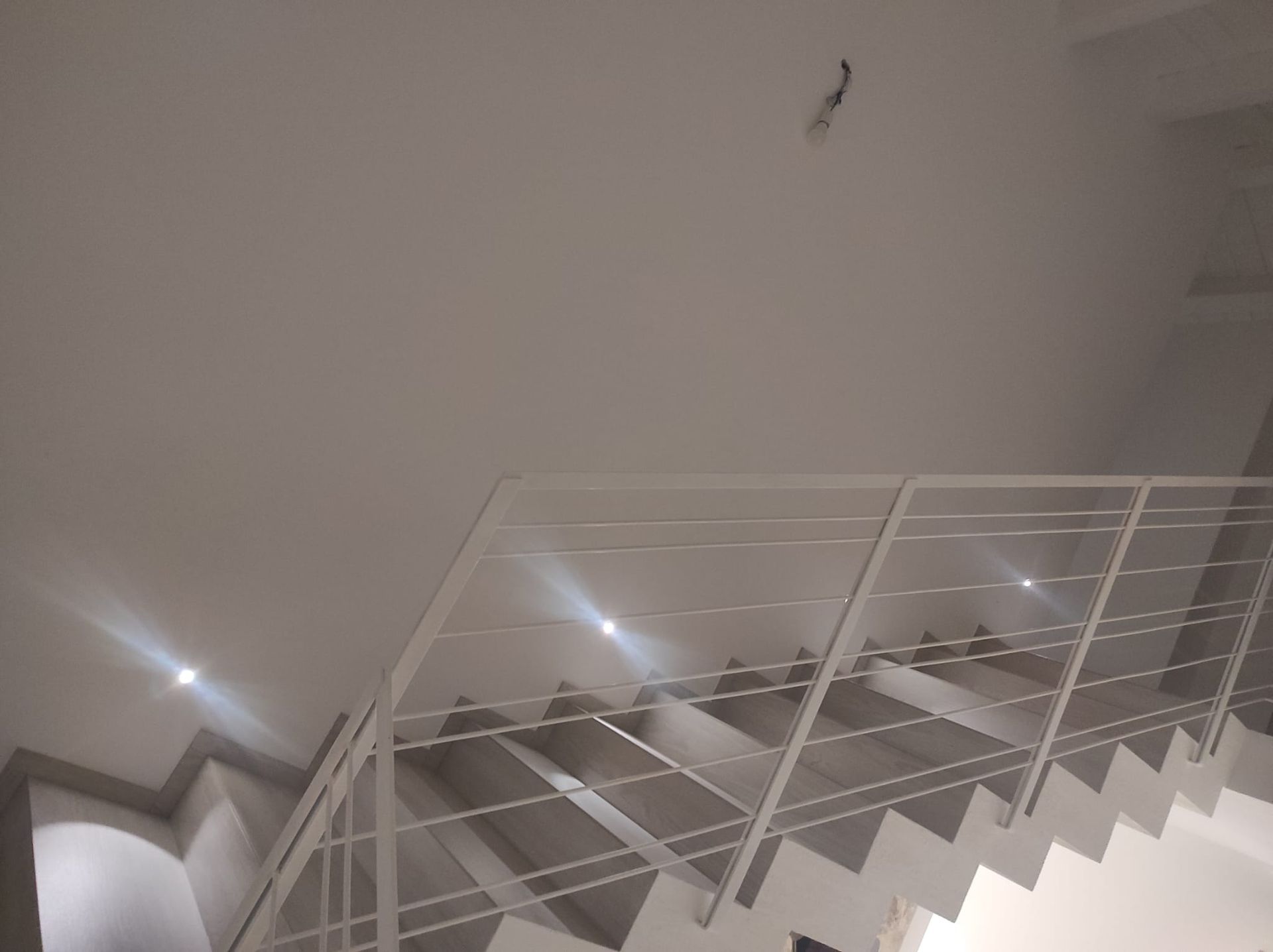 Scala interna bianca con ringhiera in metallo, vista dal basso, in un edificio moderno.