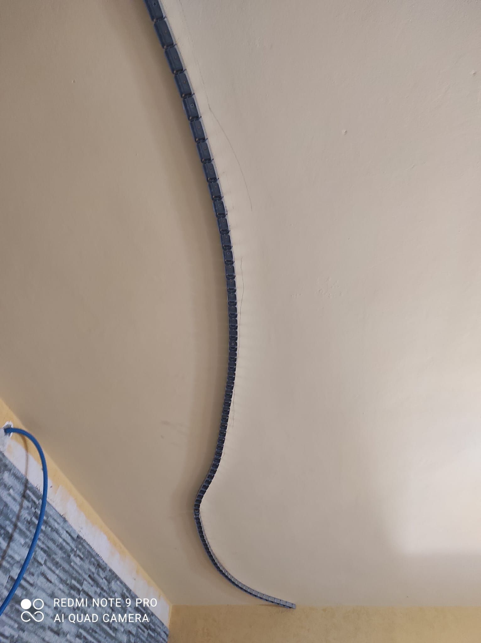 Un cavo blu arrotolato pende contro una parete beige sopra uno scaffale angolare ingombro di oggetti.