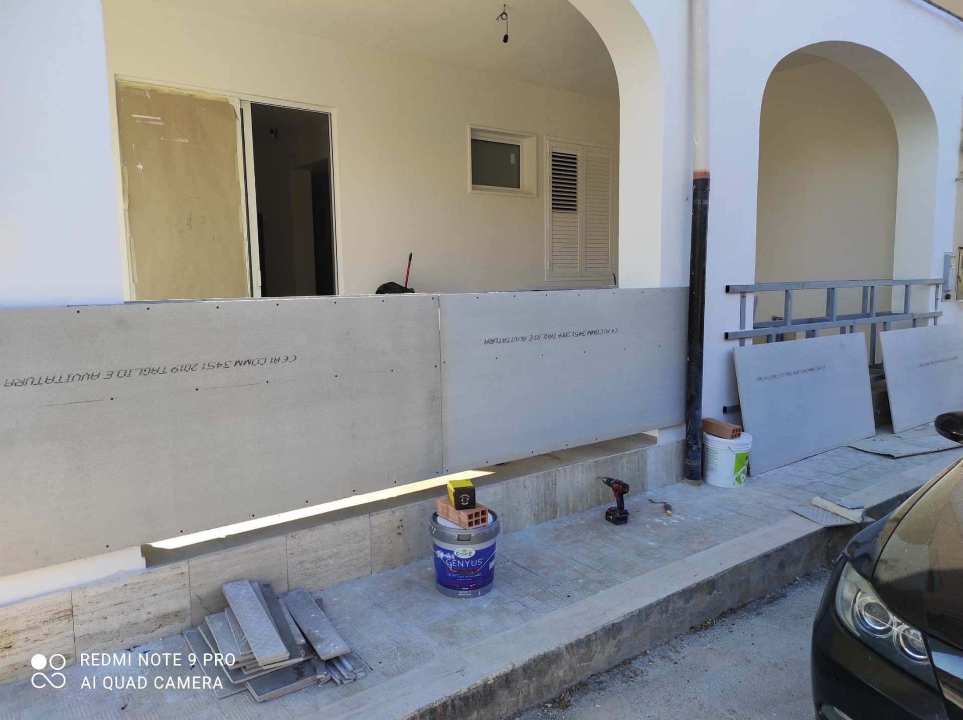Esterno di un edificio parzialmente ristrutturato con aperture ad arco, attrezzi, secchi di vernice e un'auto parcheggiata.