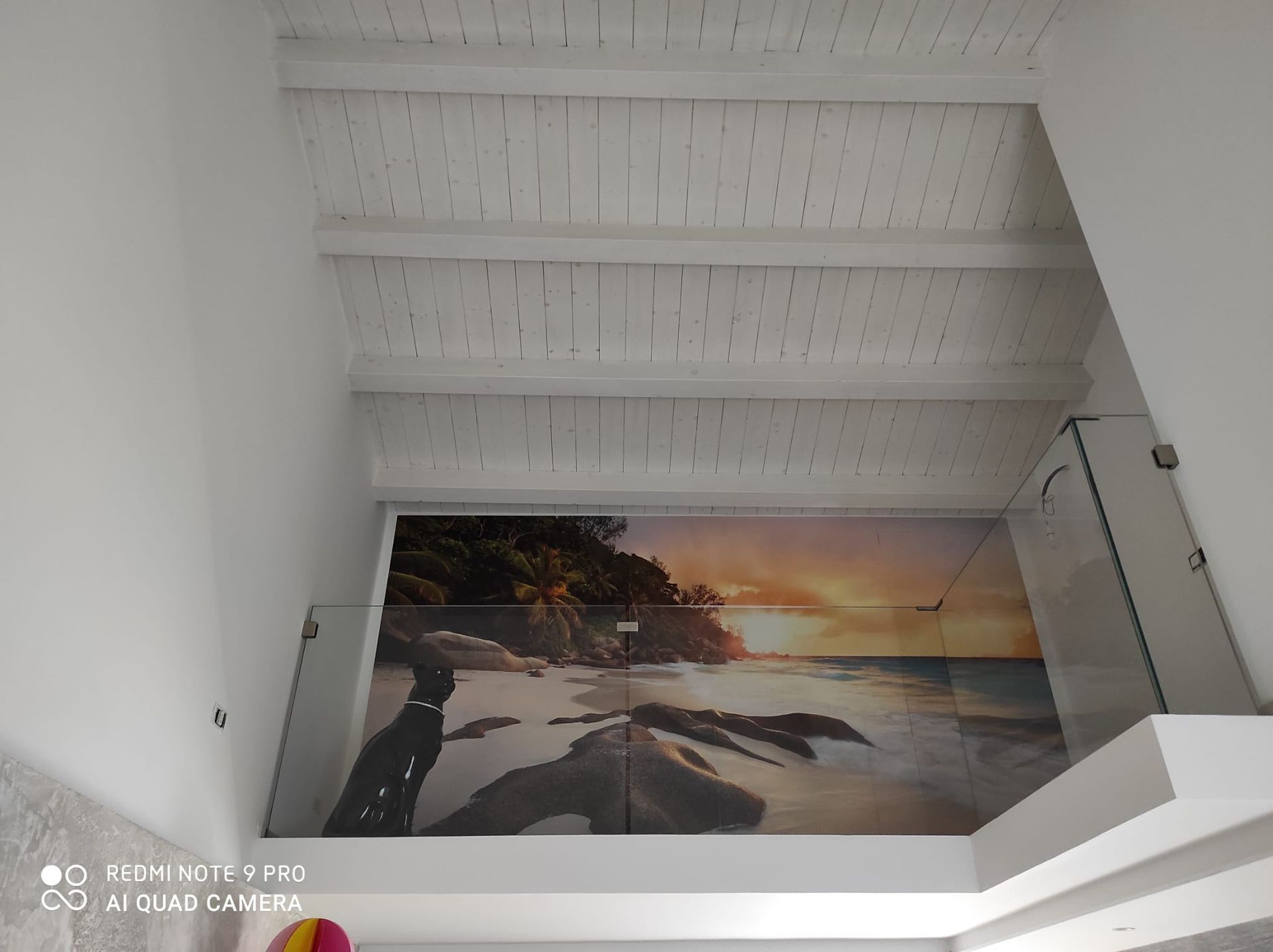 Scala bianca con un murale raffigurante un tramonto sulla spiaggia, dipinto sulla parete sotto un soffitto inclinato.