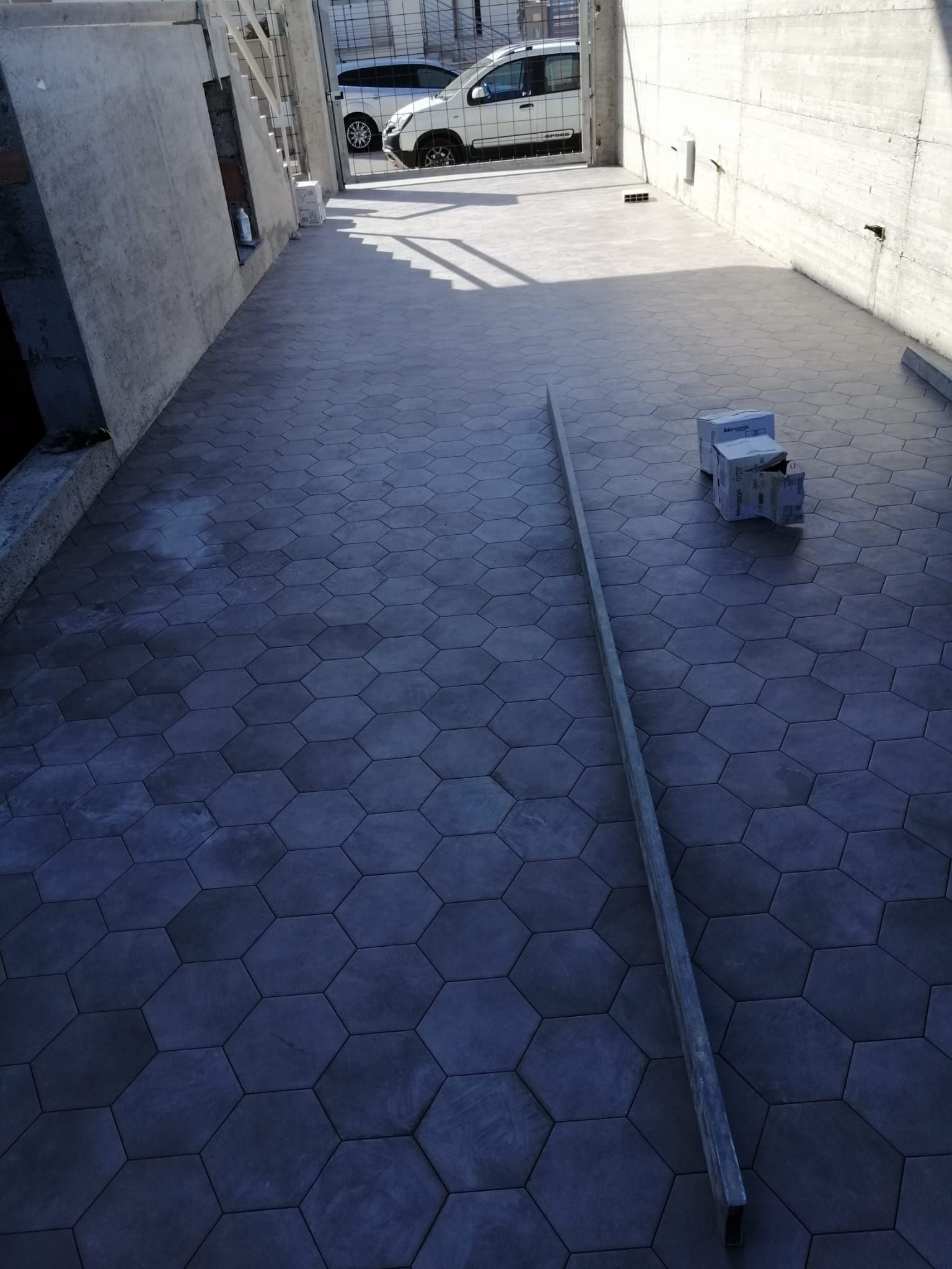 Stretto vicolo lastricato con una lunga asta di metallo a terra e un piccolo sgabello vicino a un'auto parcheggiata.