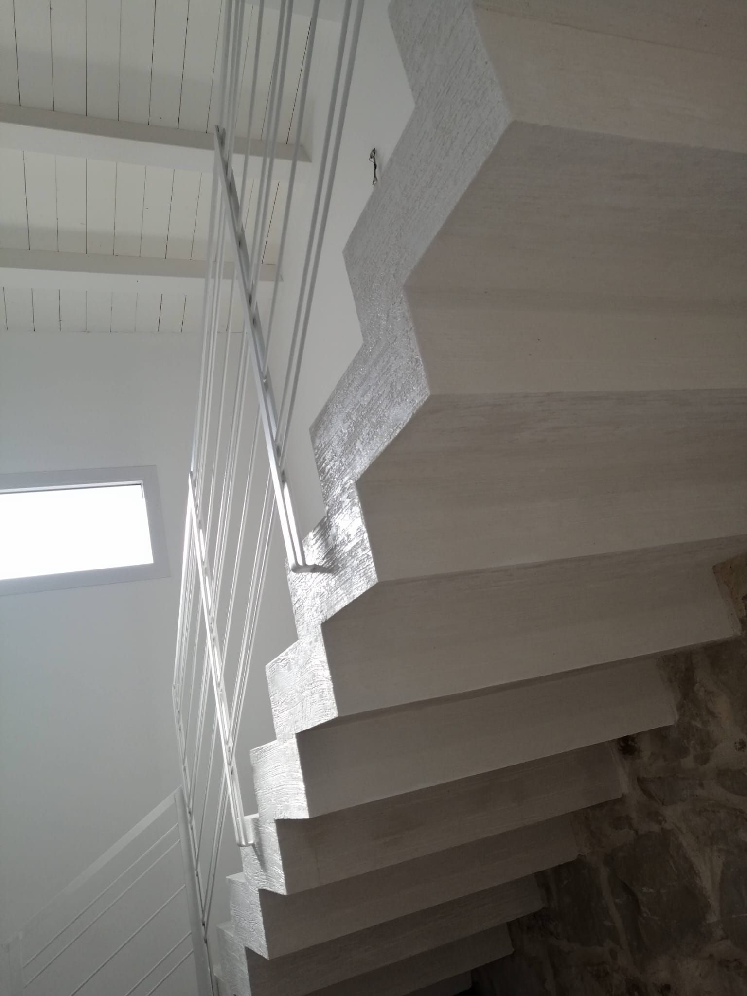 Scala moderna bianca con ringhiera in cavi metallici, vista dal basso in un interno luminoso.