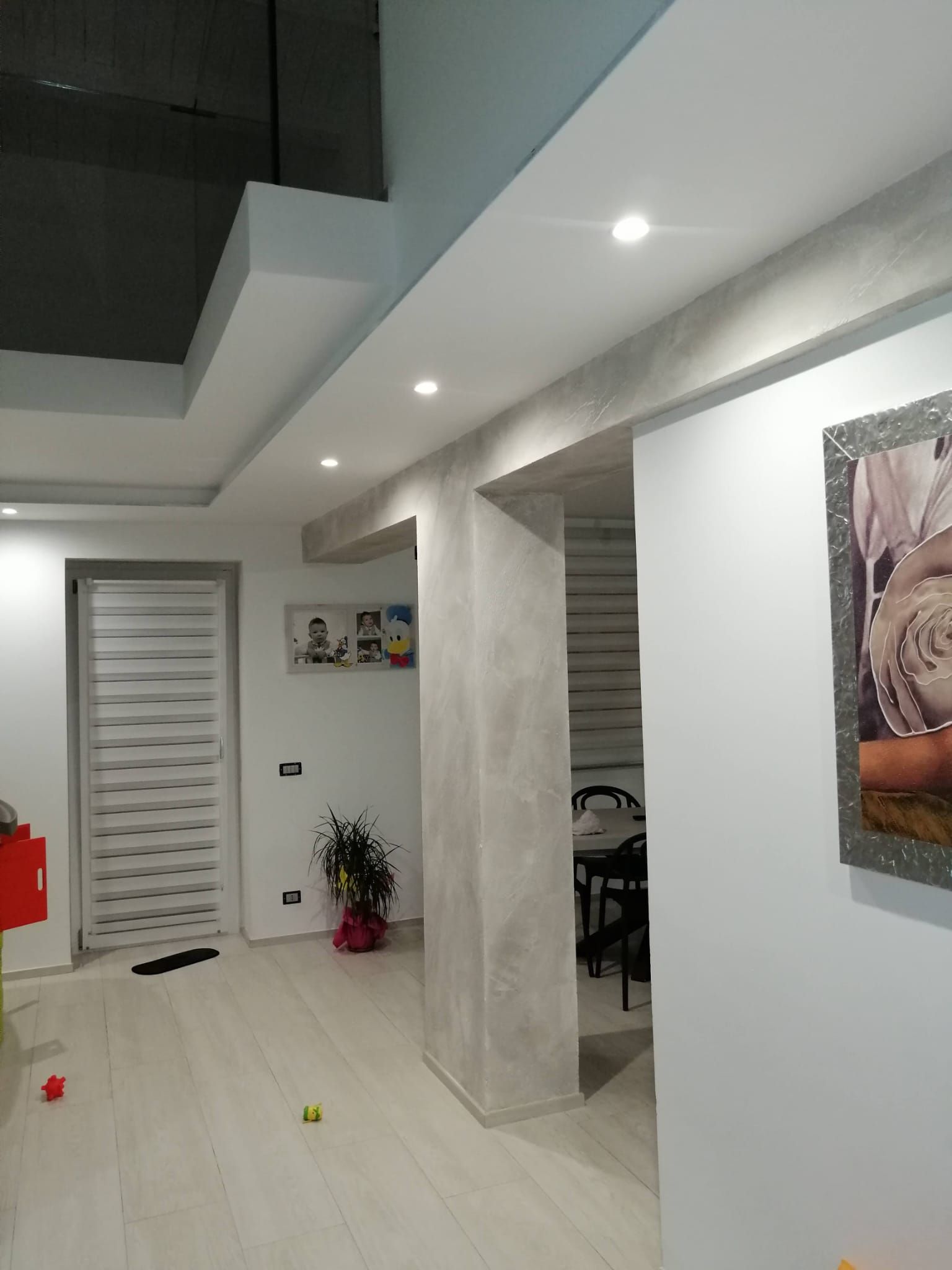 Corridoio moderno bianco con faretti a incasso a soffitto, porte a righe, una colonna centrale e opere d'arte alle pareti.