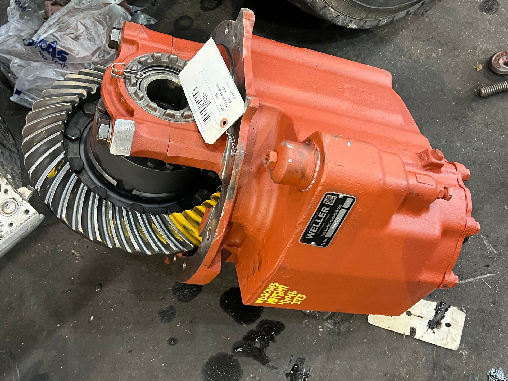 Orange heavy-duty differential with open gears, a tag attached, and a black data plate on it.