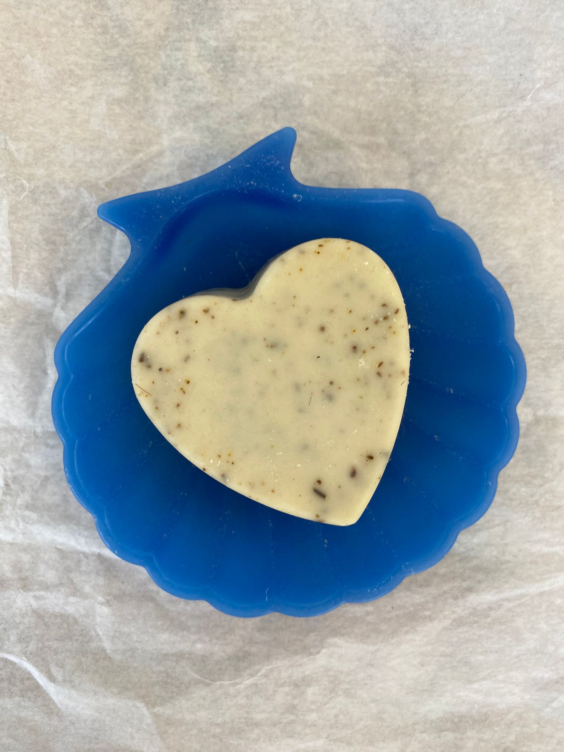 Un pain de savon en forme de cœur est posé sur un porte-savon bleu