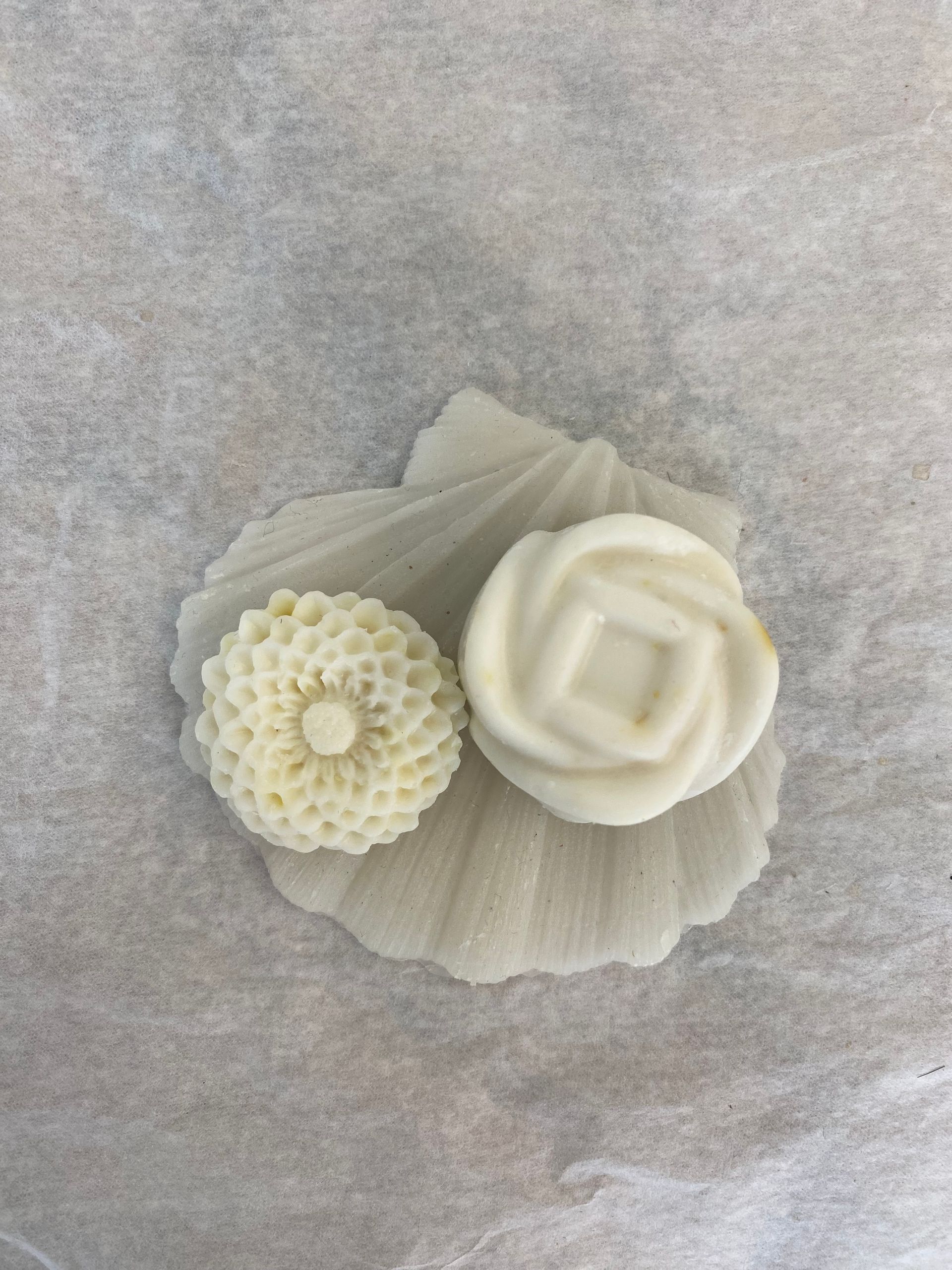 Deux savons blancs sont posés sur une coquille sur une table.