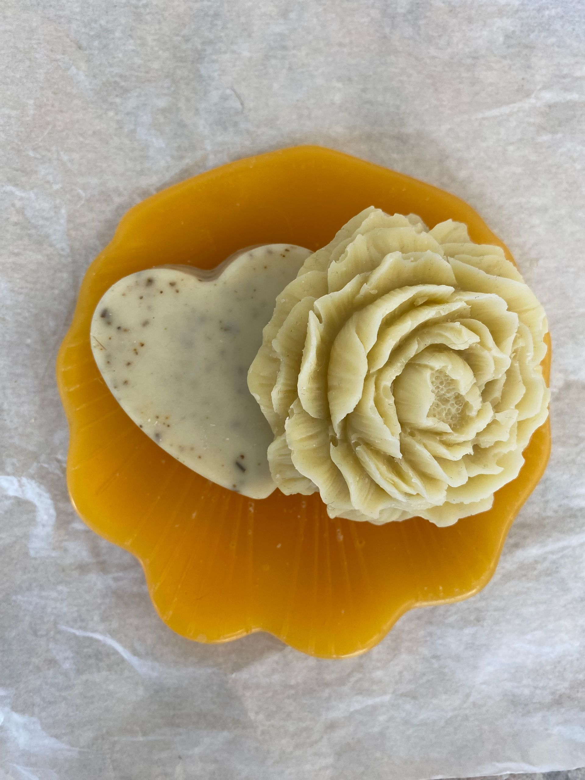 Un savon en forme de cœur et un savon en forme de fleur sont sur une assiette jaune.