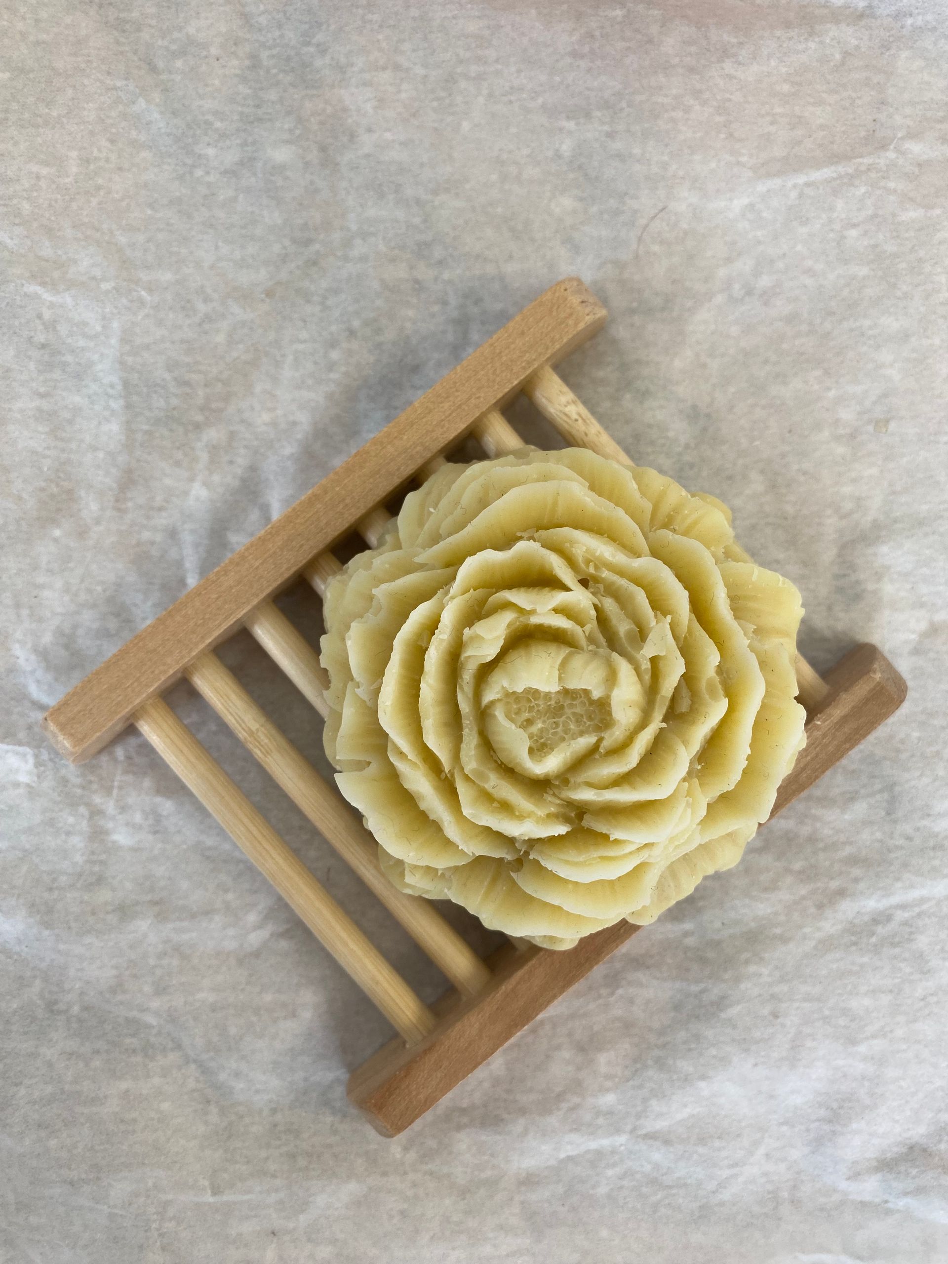 Un savon en forme de rose est posé sur un porte-savon en bois.