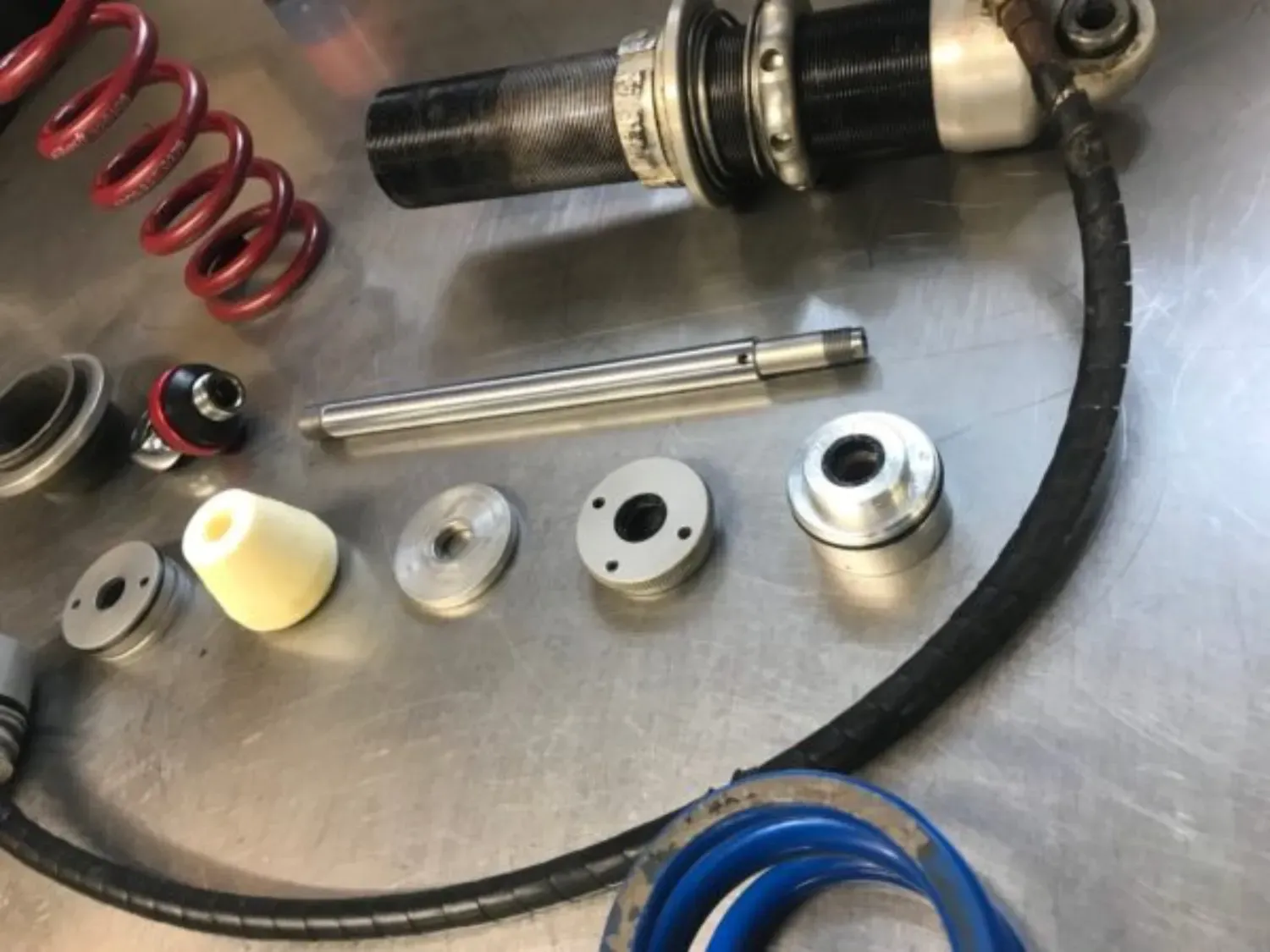 Disassembled shock absorber components, including springs, piston rod, and internal parts on a metallic surface.