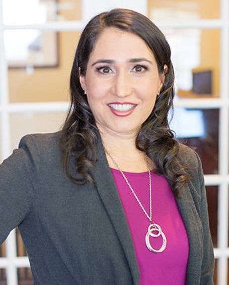 A woman wearing a purple shirt and a necklace is smiling for the camera.