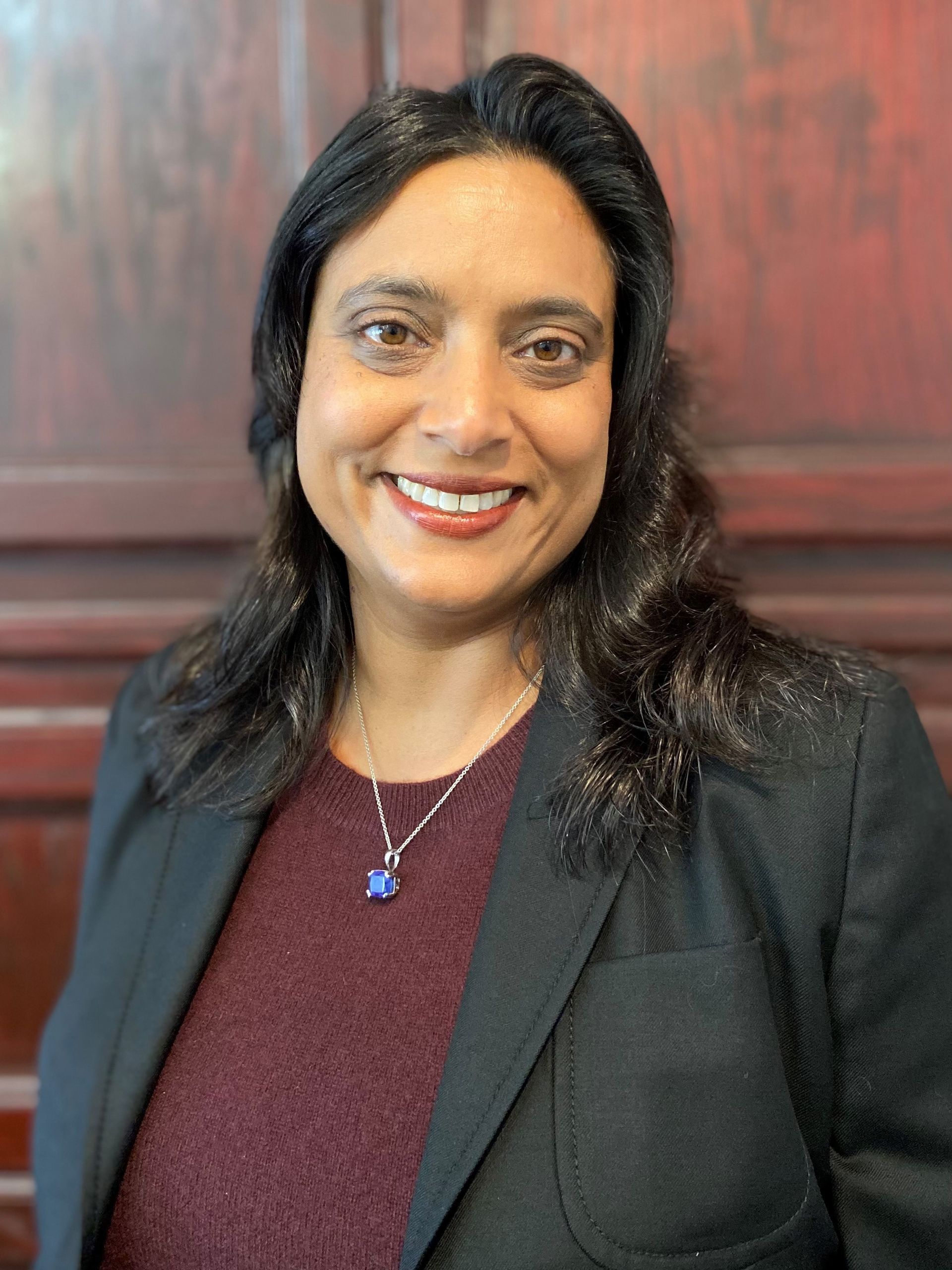 A woman wearing a black jacket and a necklace is smiling for the camera.