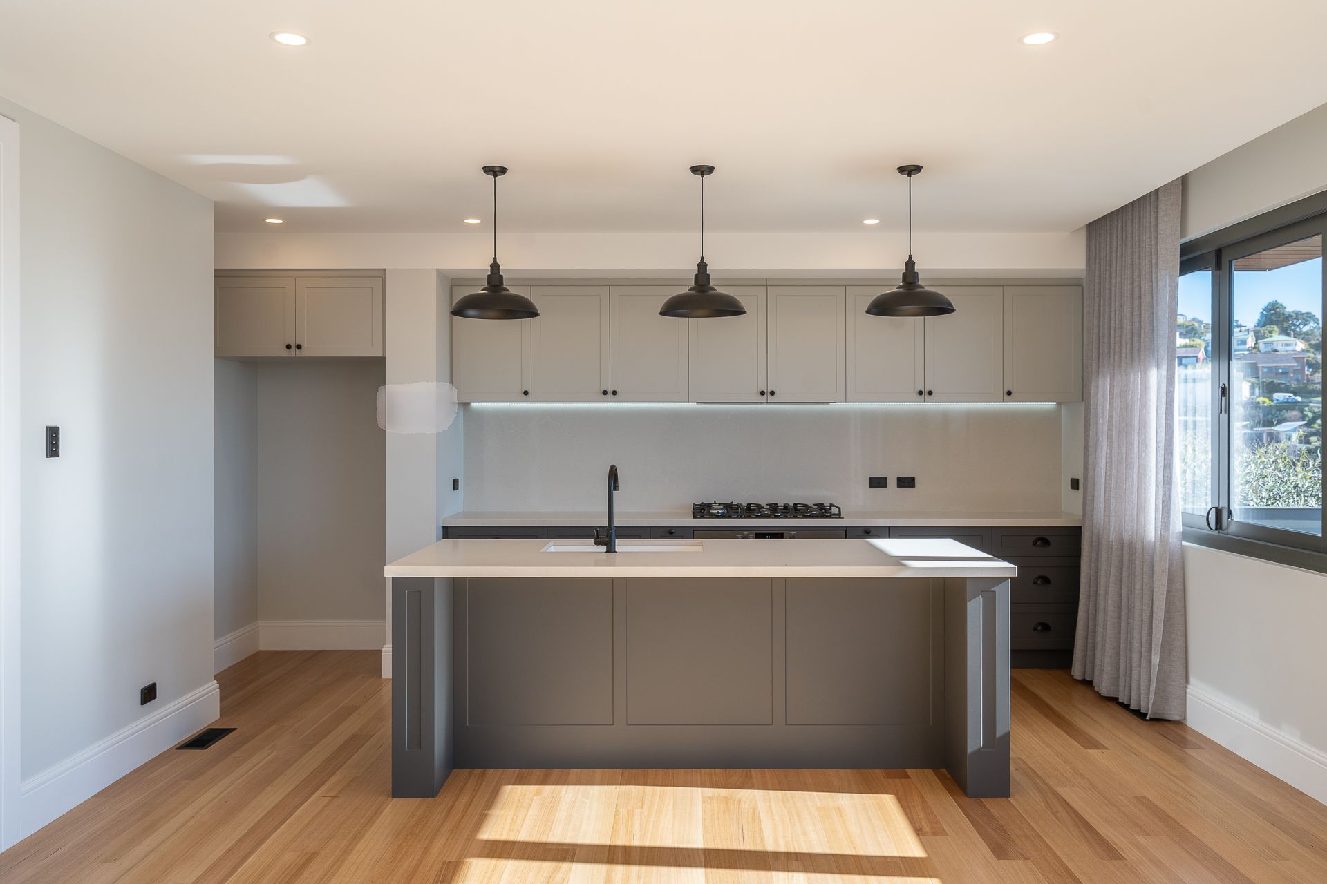 Modern kitchen with a dark stone island, black stools, black refrigerator, and a glimpse of a bedroom in the background.