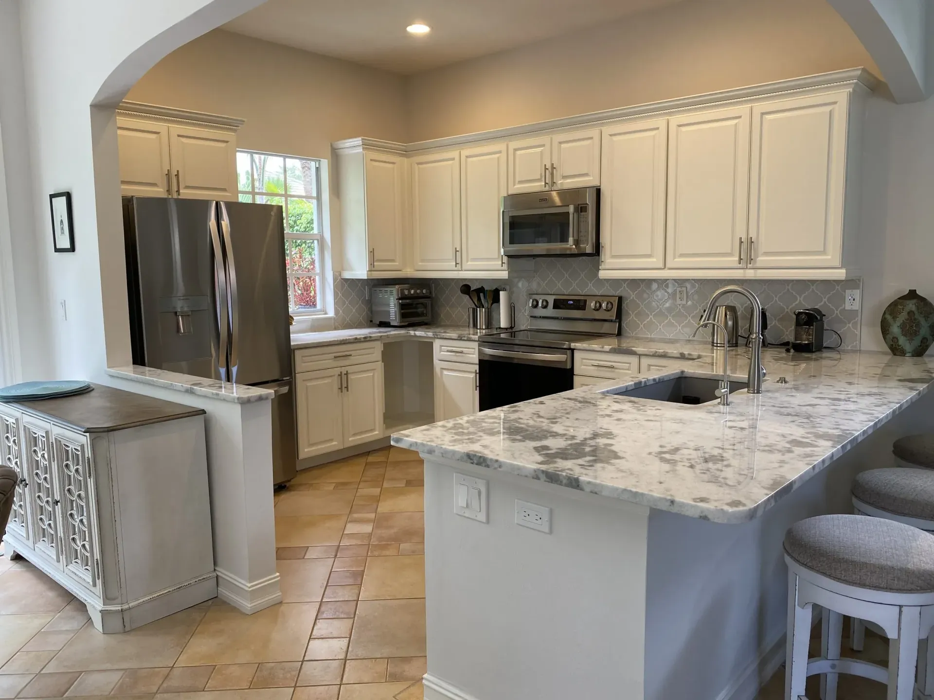 Elegant kitchen with white cabinets, dark island, granite countertops, and stainless steel appliances