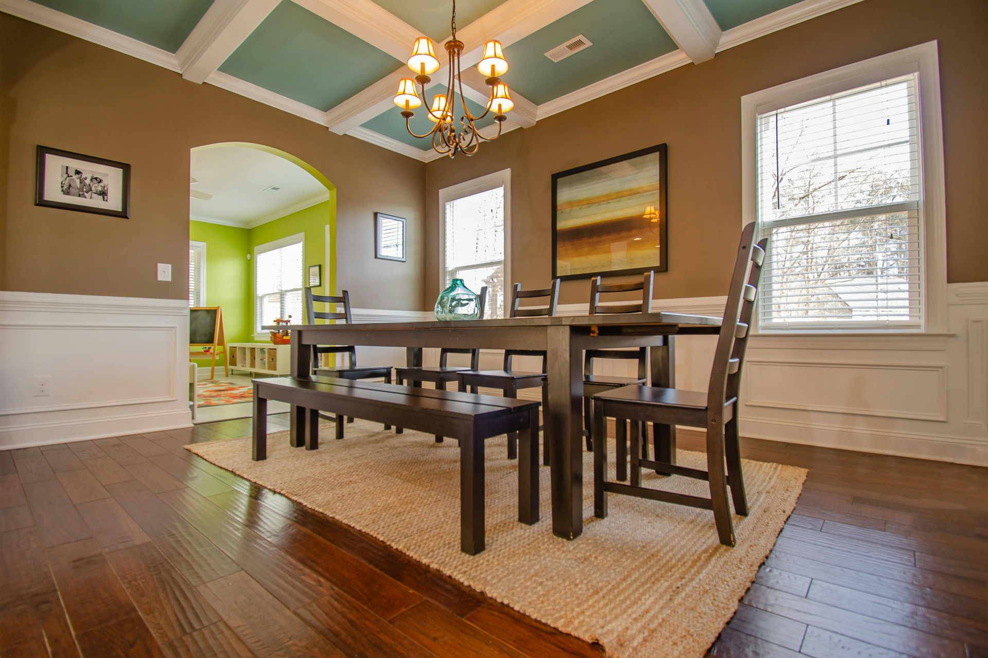 Dining room with dark wood table, teal coffered ceiling, hardwood floors, and a large rug under a chandelier