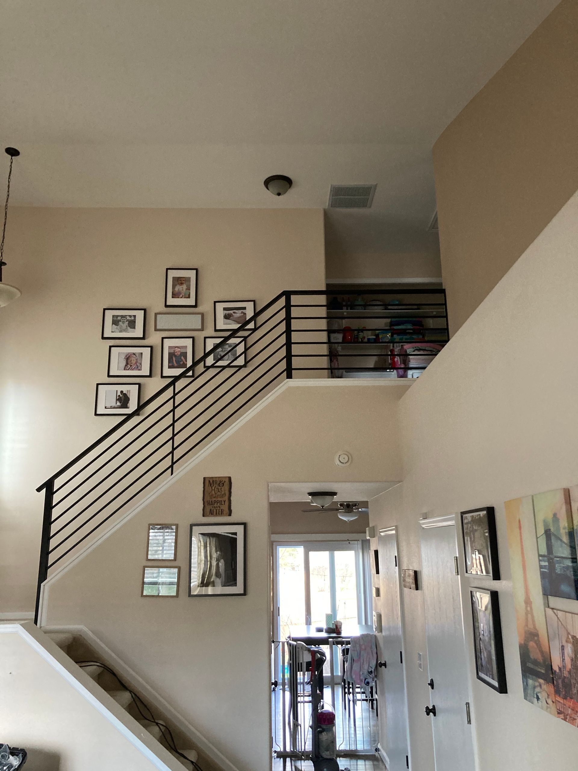 Staircase with black railing, framed photos on wall, leading to a loft area. High ceiling, neutral walls.