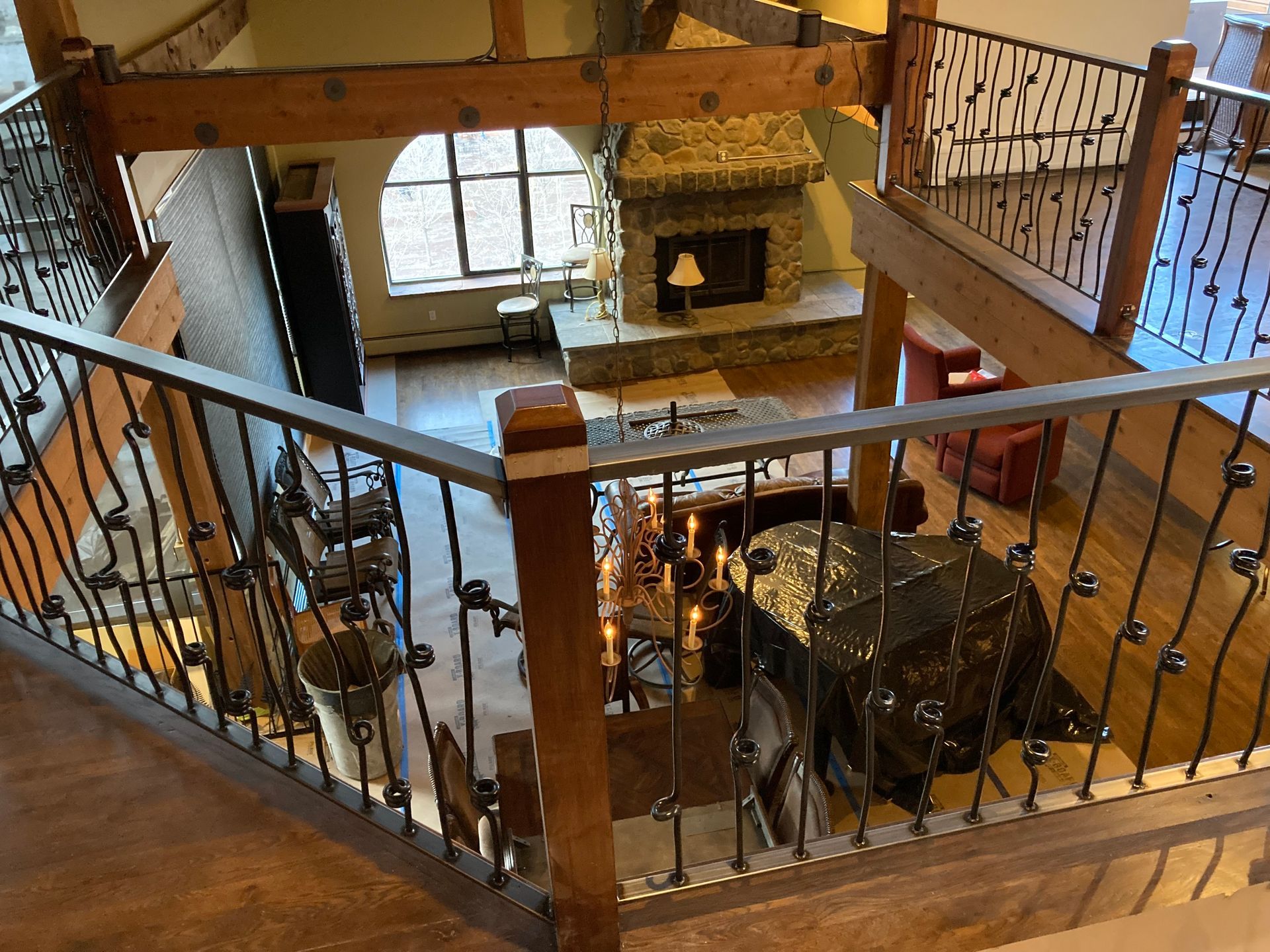 View from an interior balcony of a wooden lodge-style living room with a fireplace, staircase, and wrought-iron railings.
