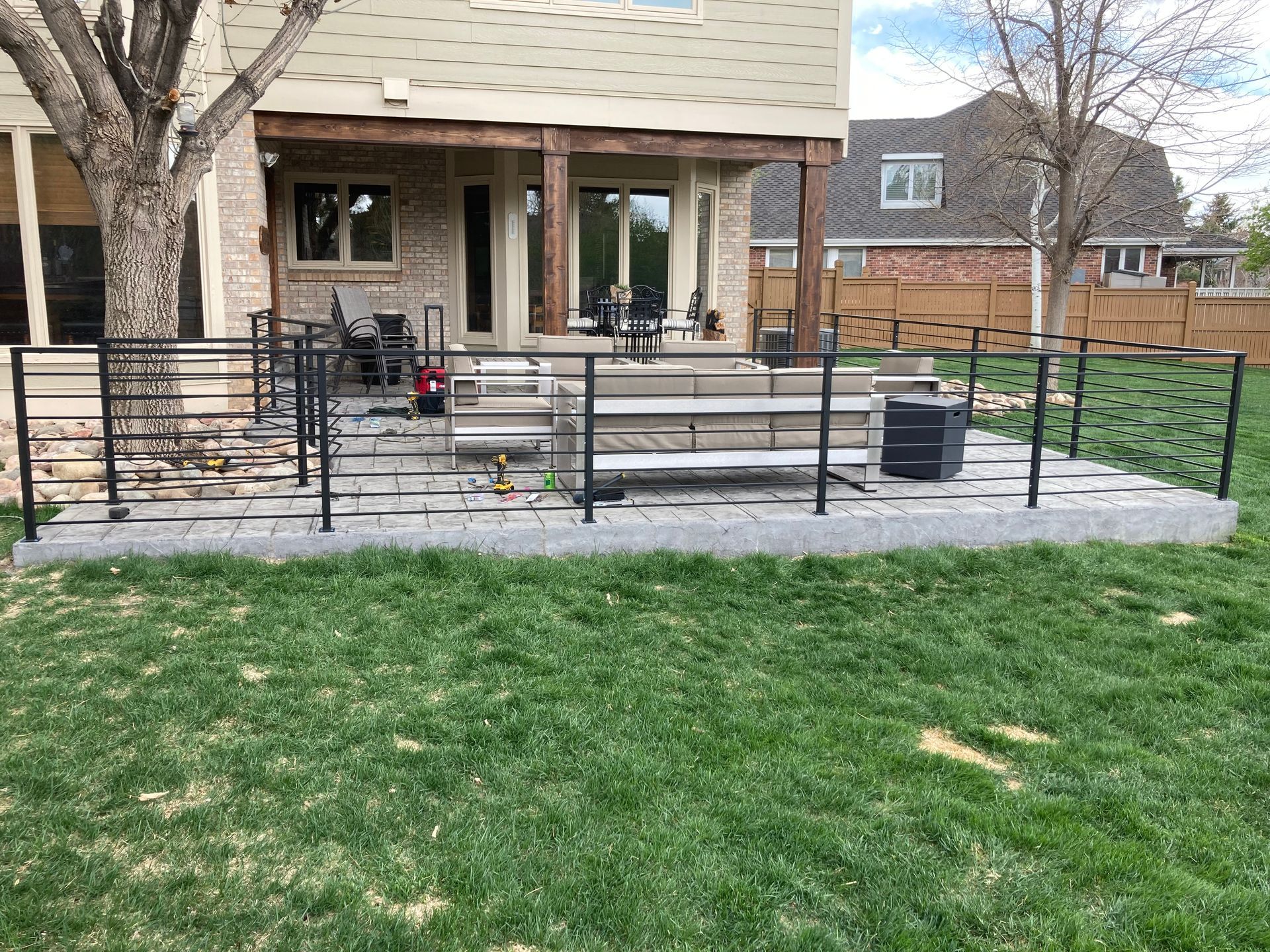 Backyard patio with black railings, concrete blocks, and green grass.