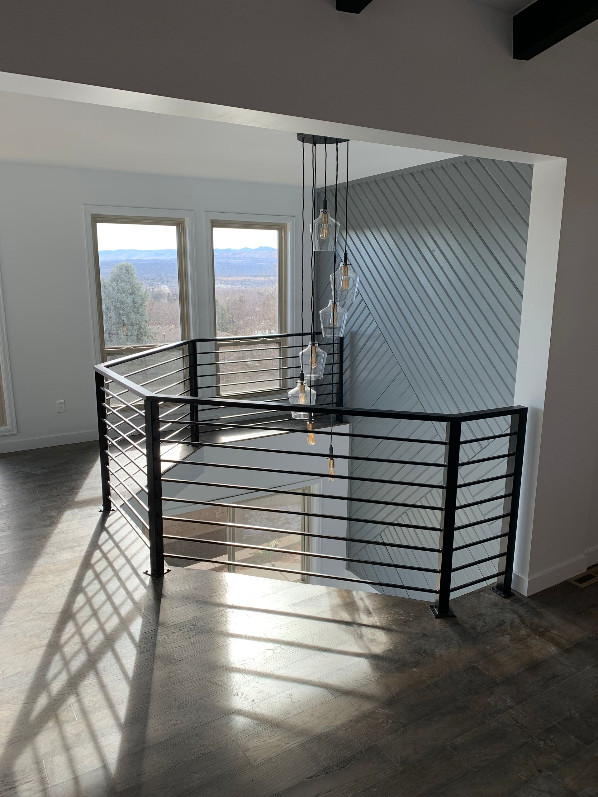 Black metal railing on a staircase landing with a view through windows. Sunlight casts shadows on the floor.
