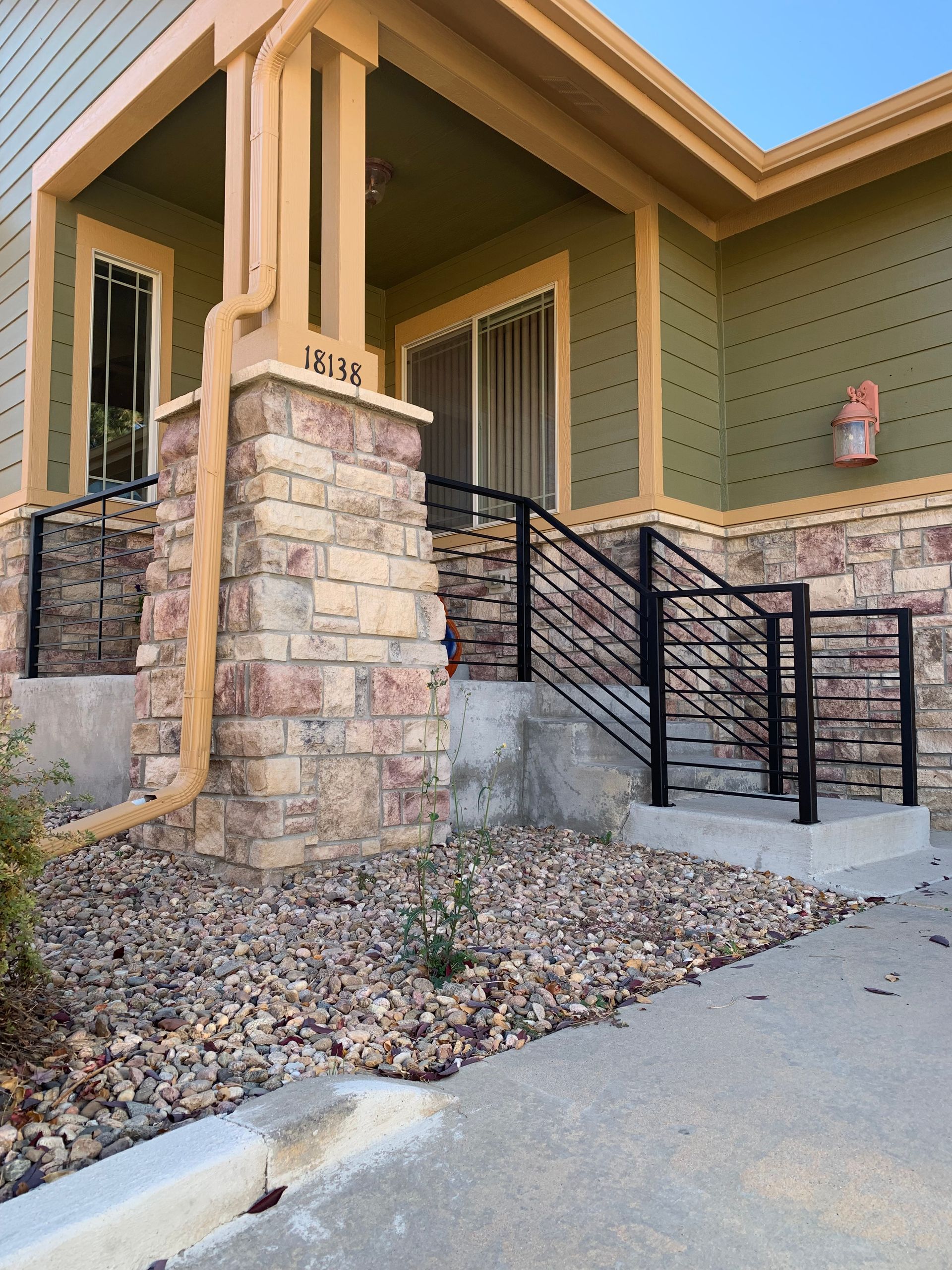 Exterior of a building with stone columns, stairs, black handrails, and a gravel yard.