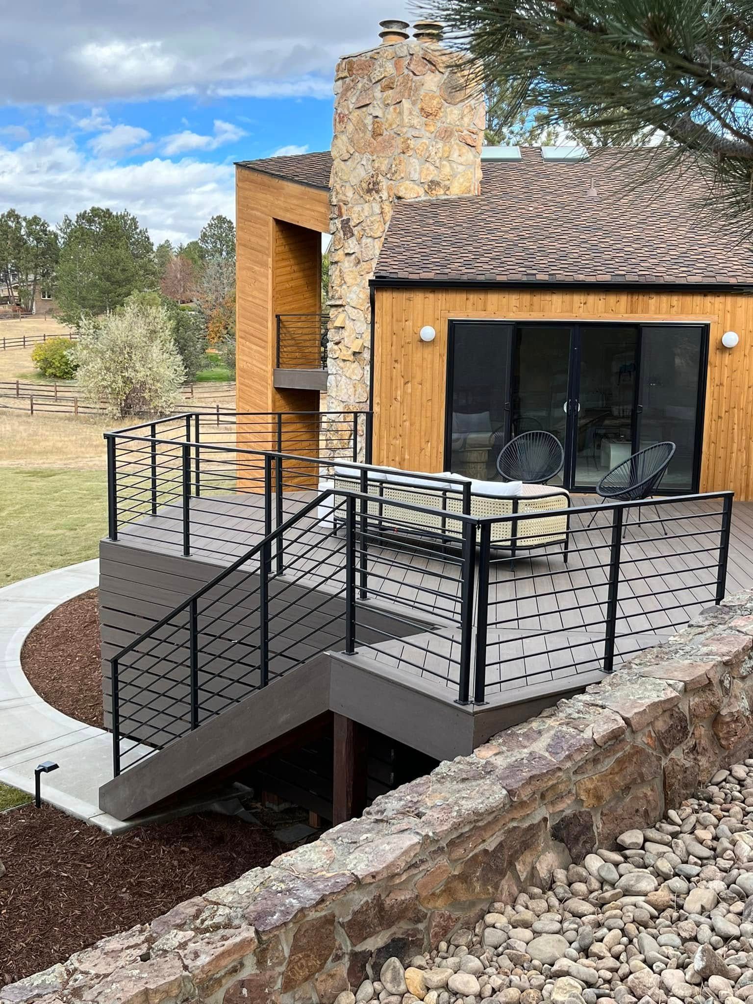 Wooden deck with black railing, leading to a building. A chimney is to the left.