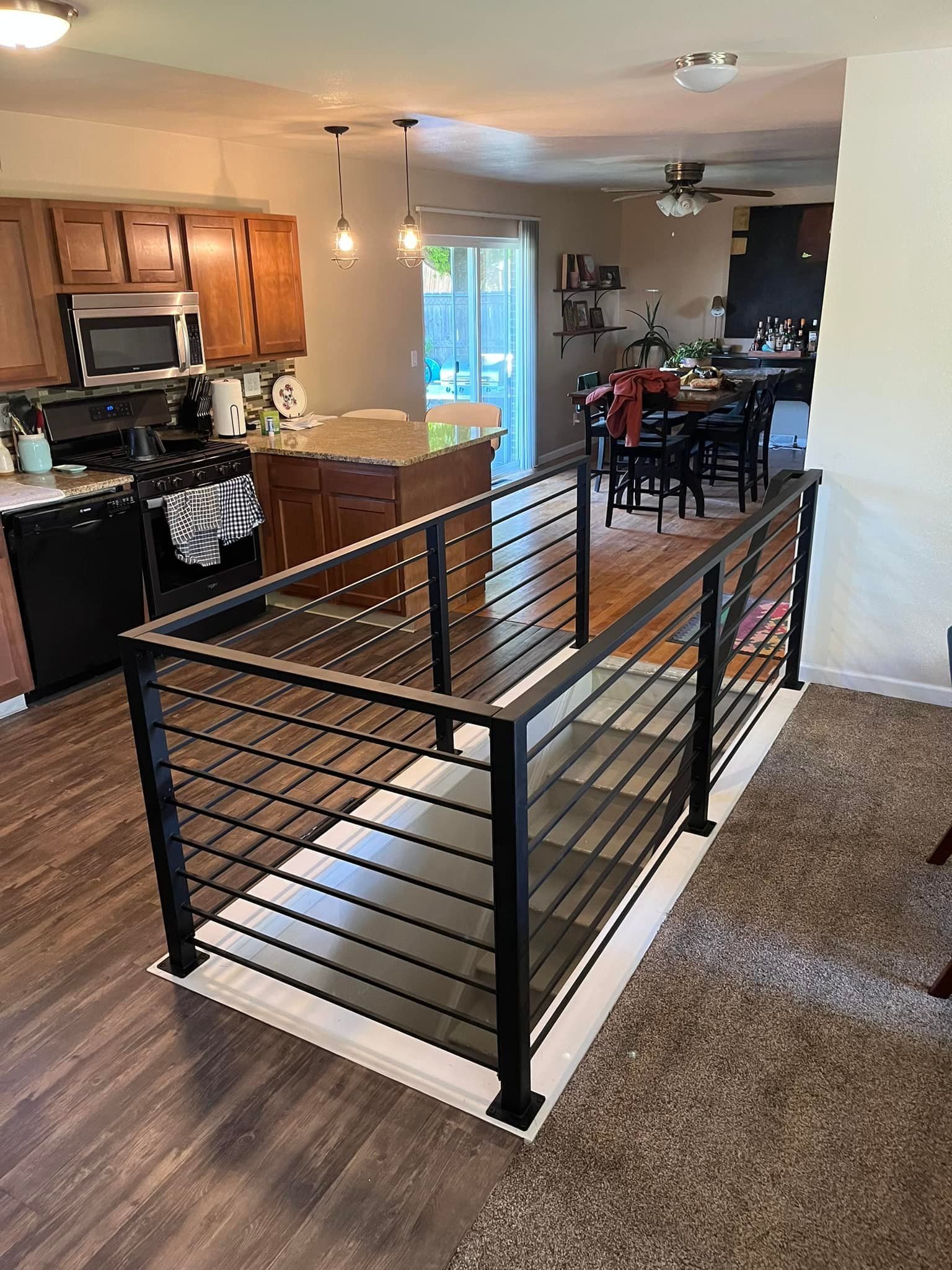 Black metal railing around a recessed staircase. Kitchen and dining areas visible.