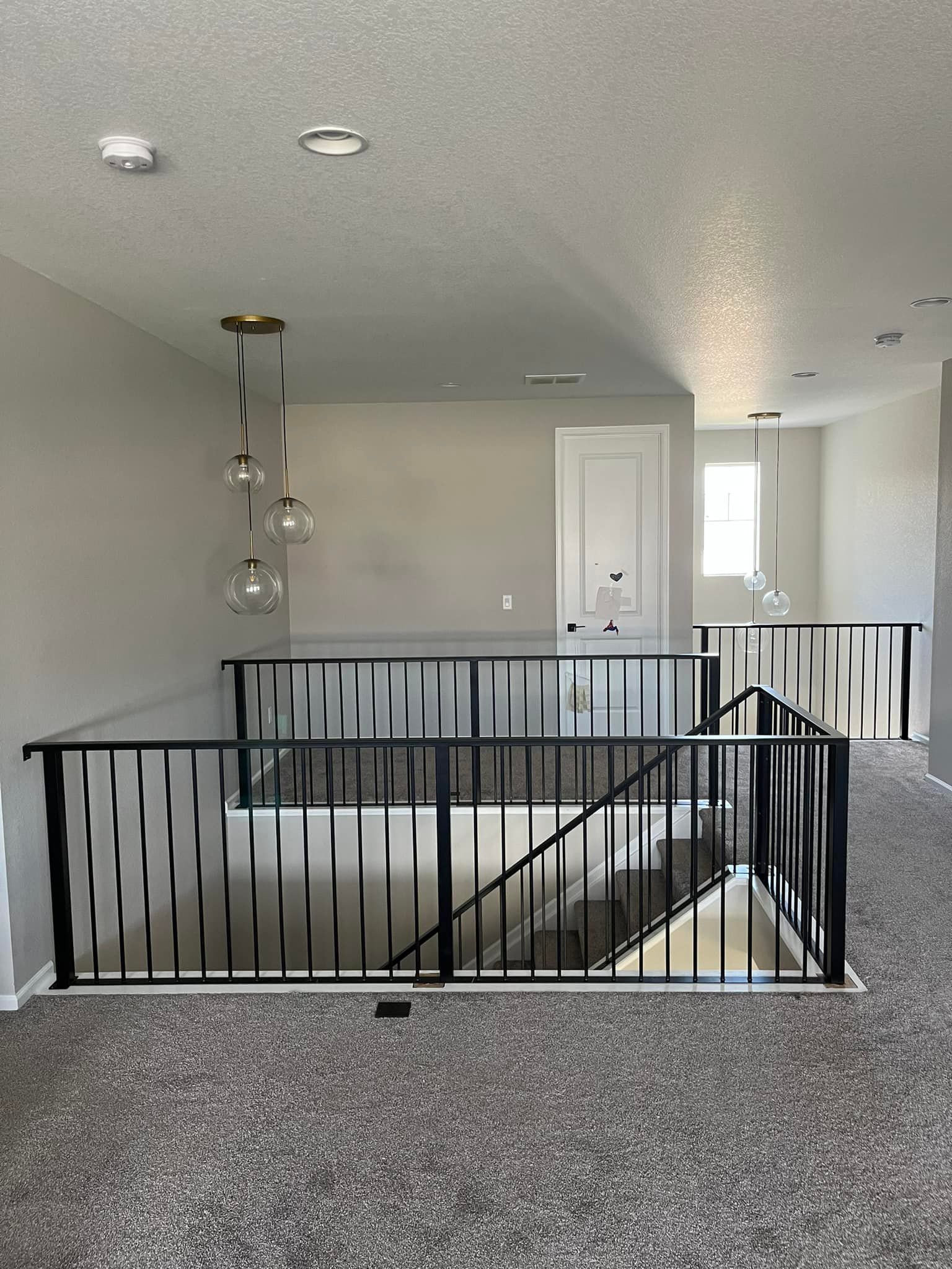 Loft area with black railing, gray walls, and pendant lights. Carpeted floor, doorway at the end.