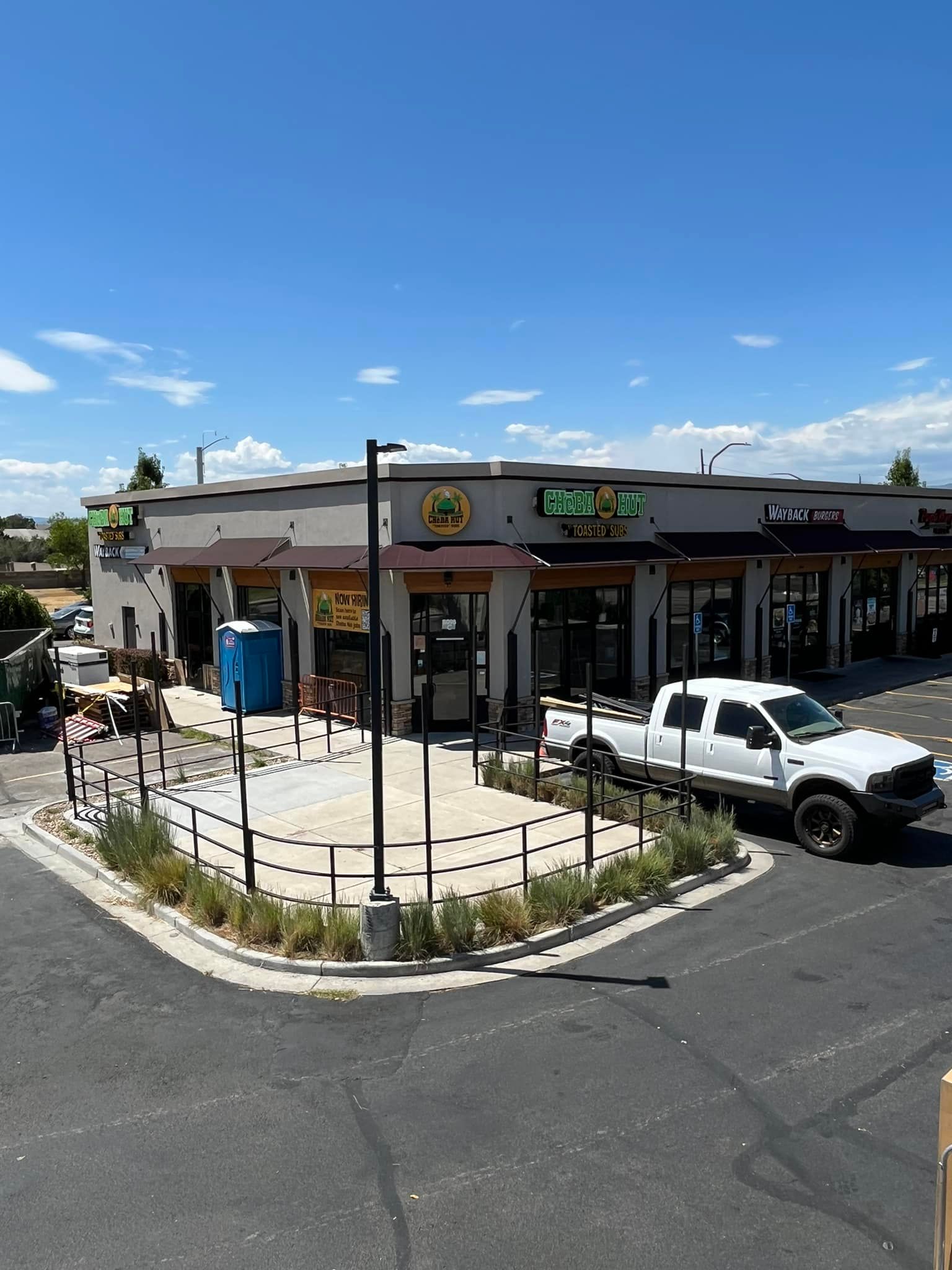 Restaurant exterior with seating area, white truck parked out front on a sunny day.