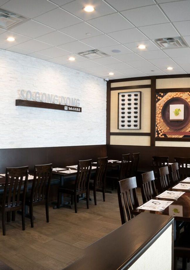 Empty restaurant dining area with dark chairs, wooden tables, and wall art under bright ceiling lights