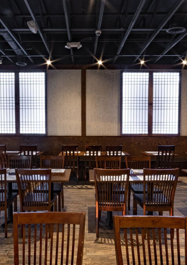 Empty wooden chairs in a dimly lit dining hall with large windows and a high dark ceiling