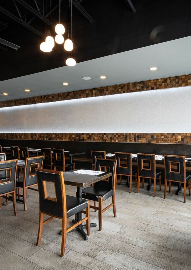 Modern café interior with empty tables, wooden chairs, and pendant lights above a long white wall