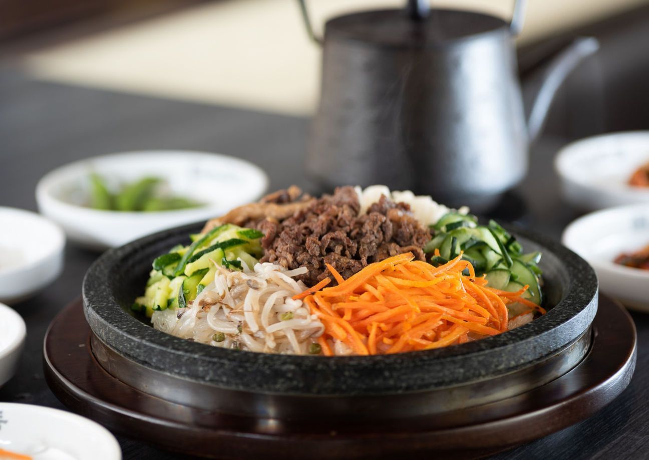 Bibimbap in a hot stone bowl topped with vegetables, beef, and sesame seeds on a table